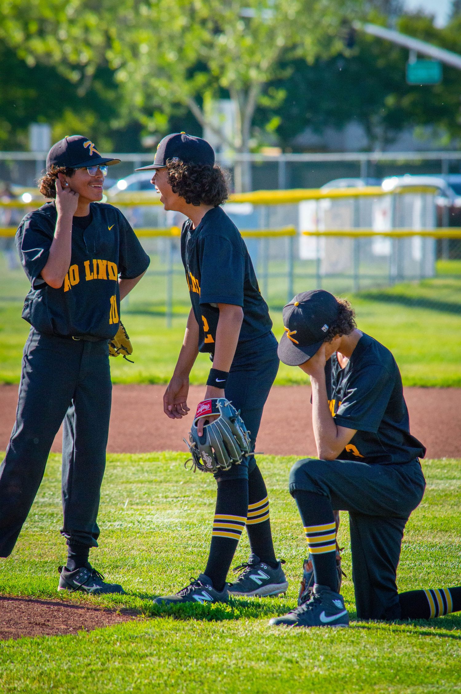 High school baseball team in dark uniforms kneeling on grass field during practice.