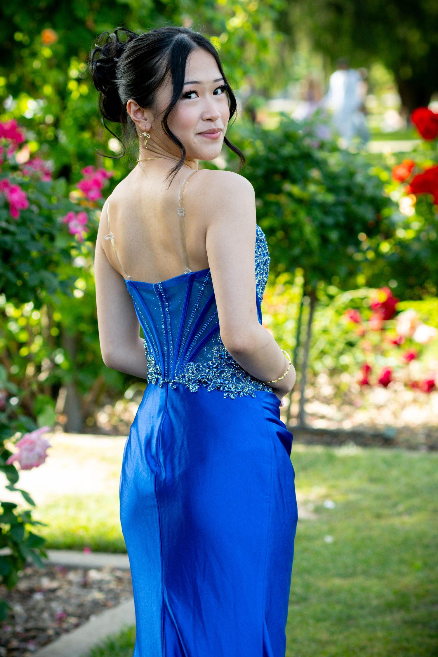 Young woman in blue beaded strapless prom gown posing in a garden with colorful roses.