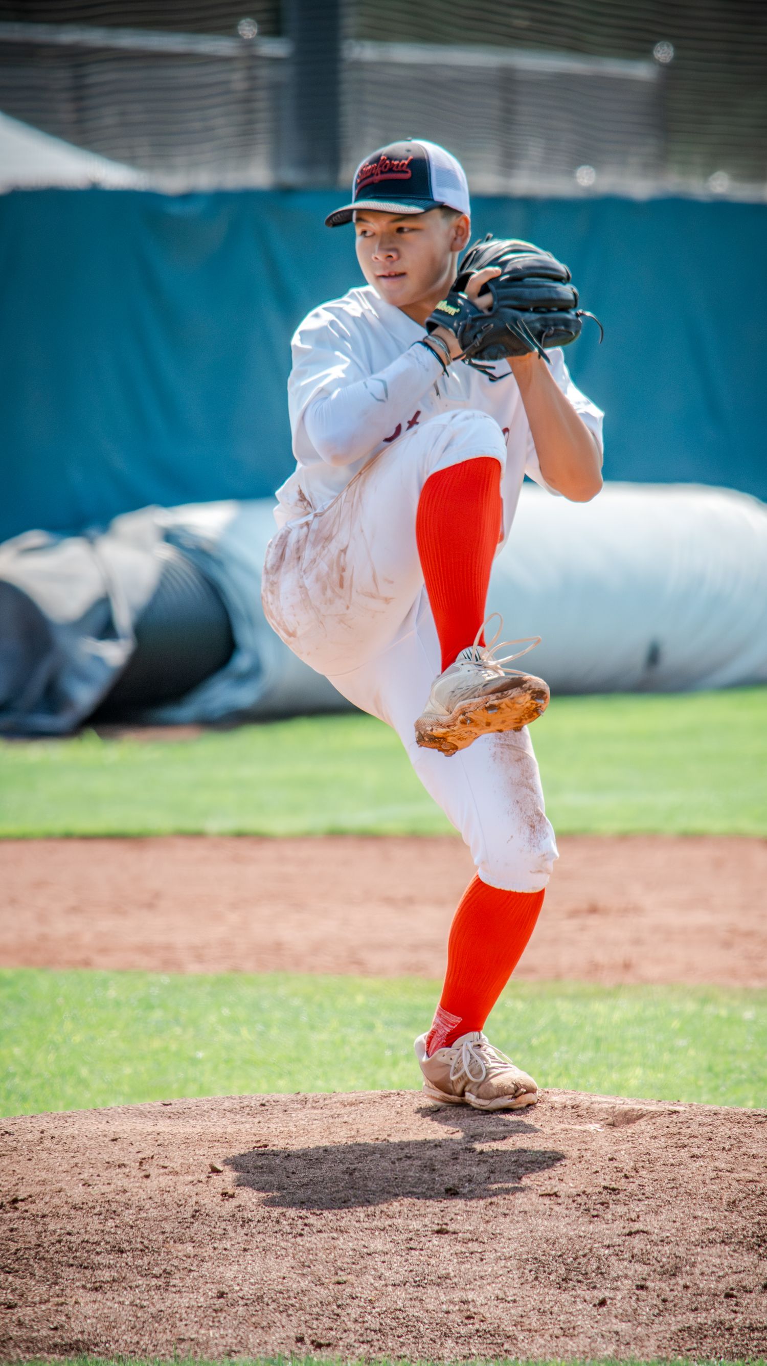 Baseball pitcher in white uniform and red socks in mid-delivery stance on pitching mound during daytime game.