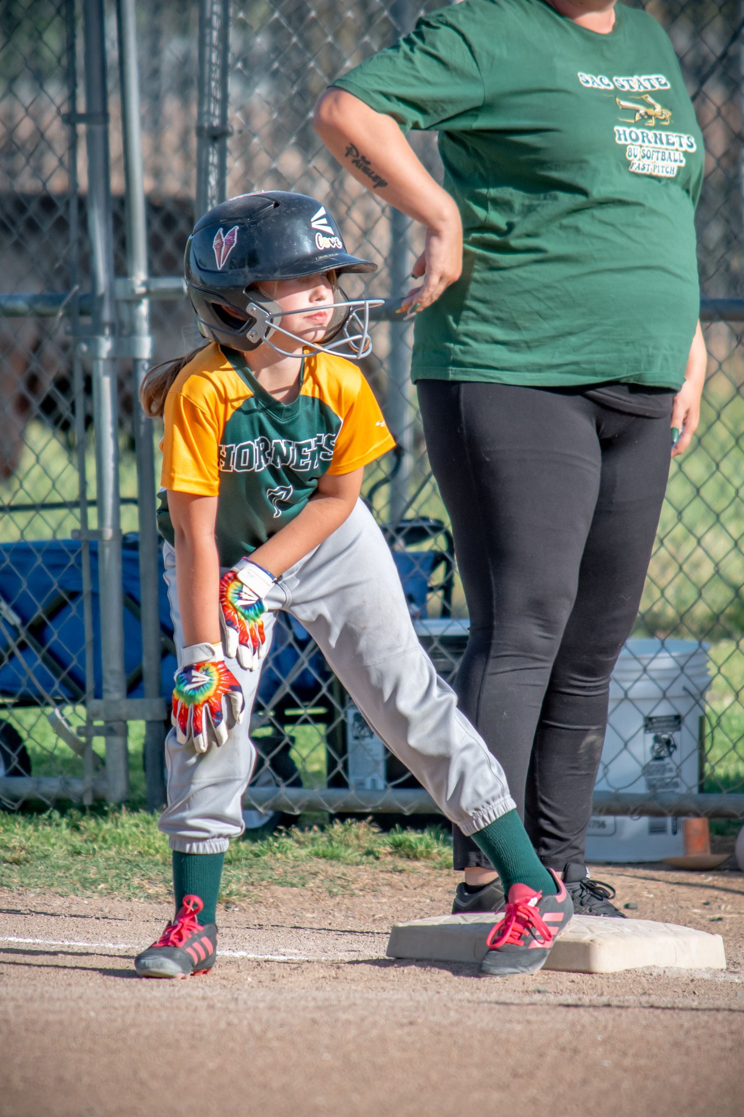 Young Softball player in baseball uniform crouching near dugout during game.