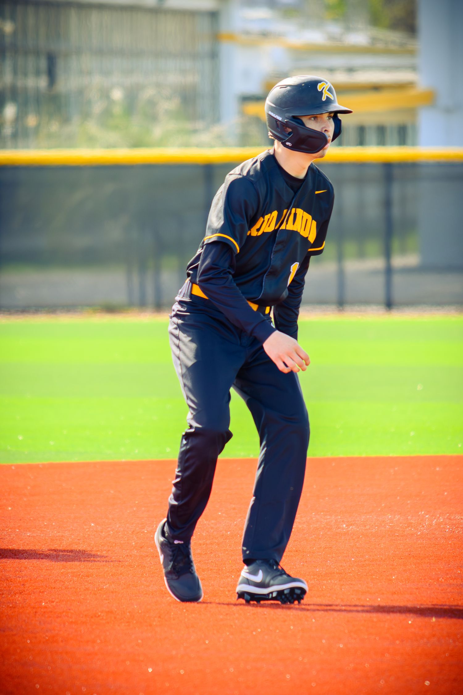Baseball player in navy uniform makes a fielding motion on bright orange artificial turf.