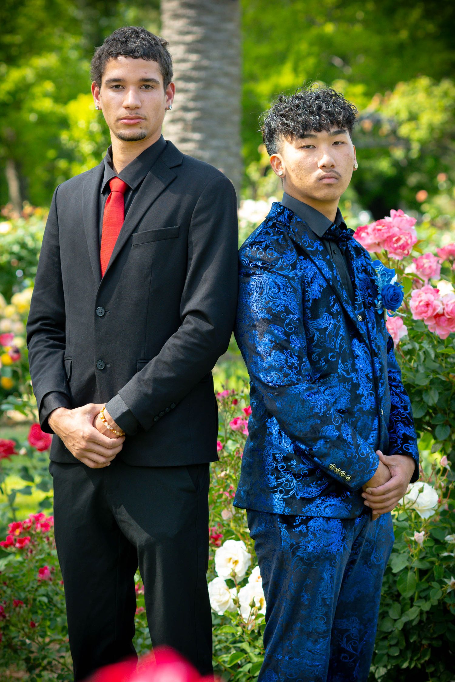 Two teenage boys in formal suits posing in a rose garden for prom photos.