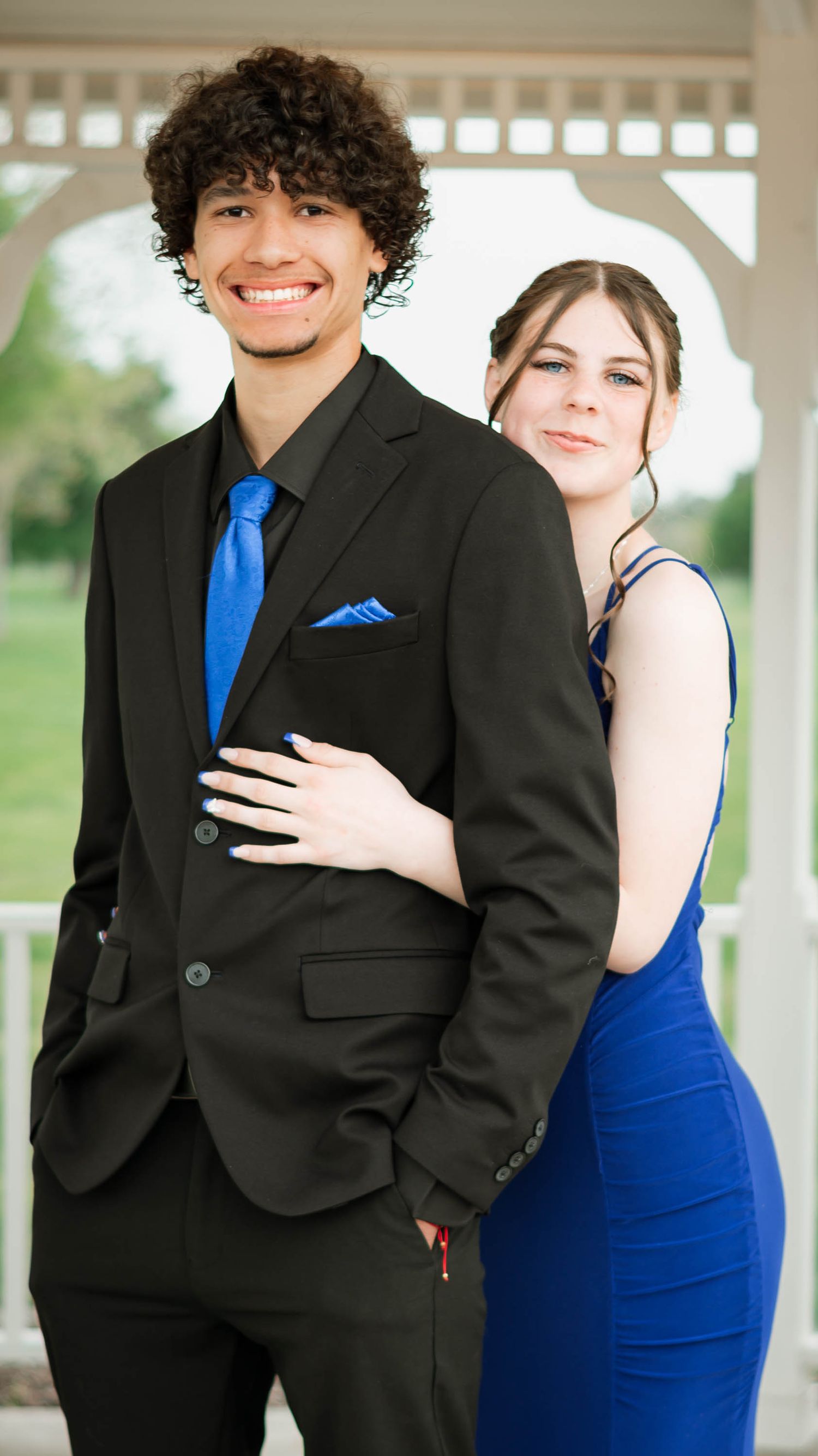 Couple in black suit and blue dress posing in white gazebo.