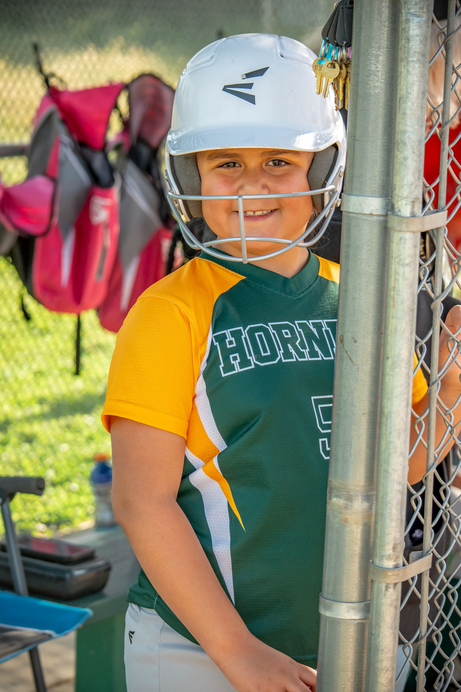 Youth Softball player in dugout wearing helmets and green team uniforms.