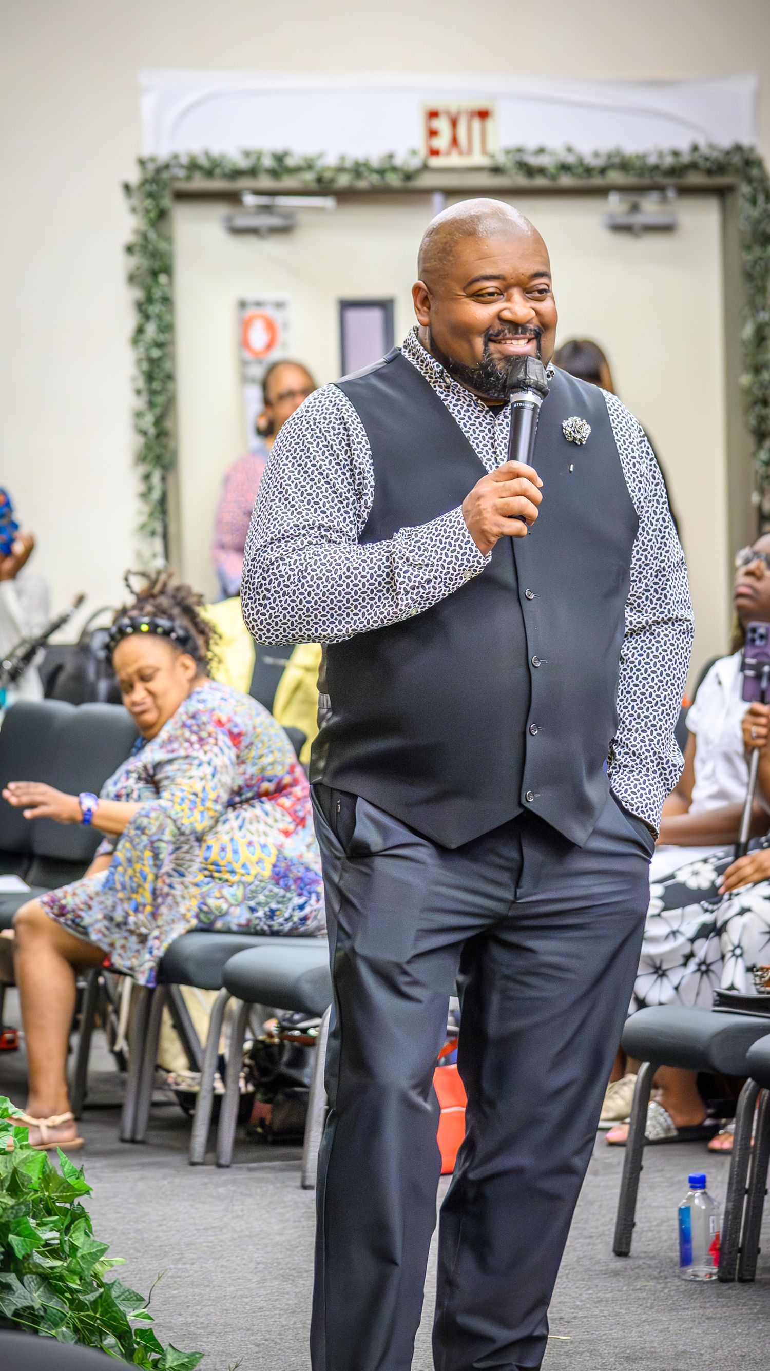 Person in formal vest and dress shirt speaking passionately into microphone at church event.