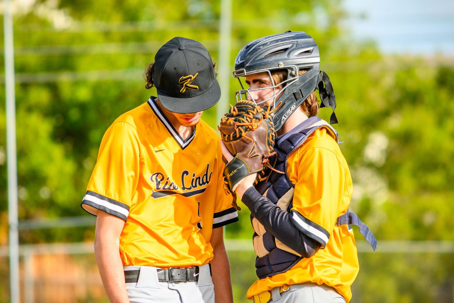 Baseball teammates in yellow jerseys gather for a discussion.