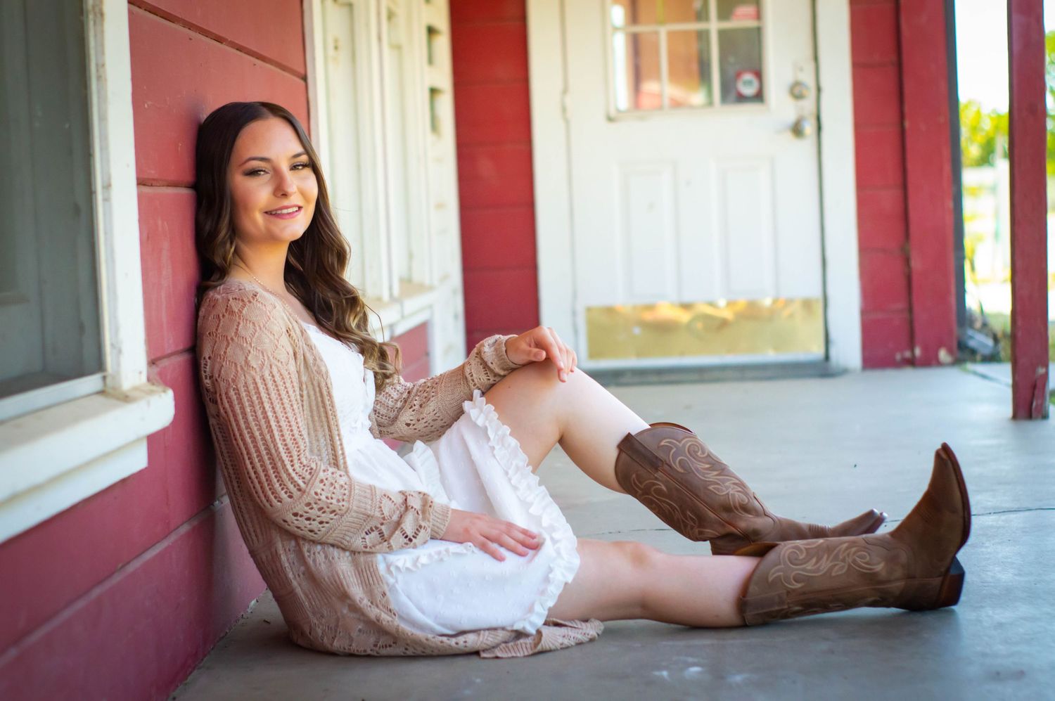 Sitting on rustic porch steps wearing cowboy boots and casual outfit.