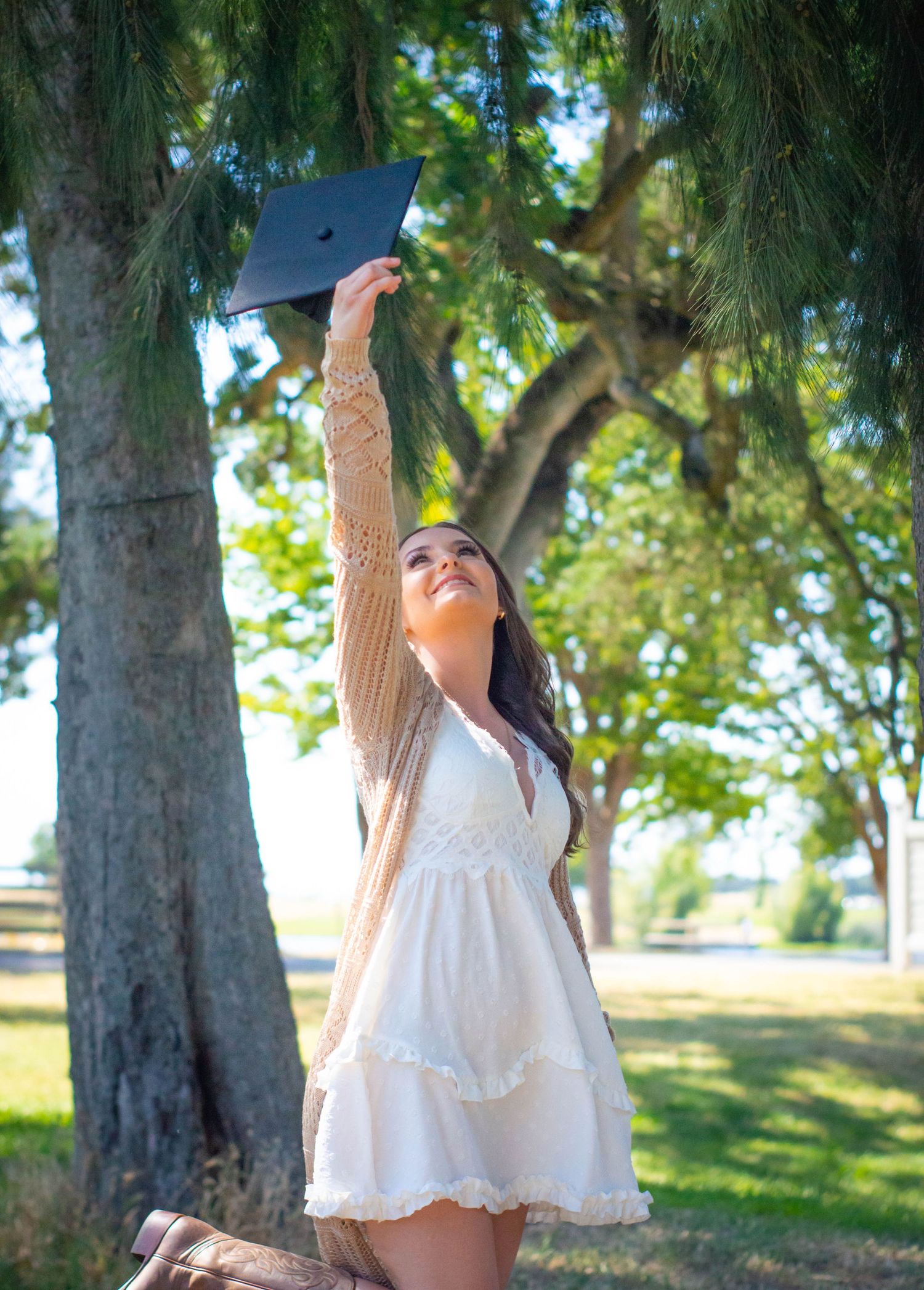 Outdoor graduation photos under trees in white sundress on sunny summer day.
