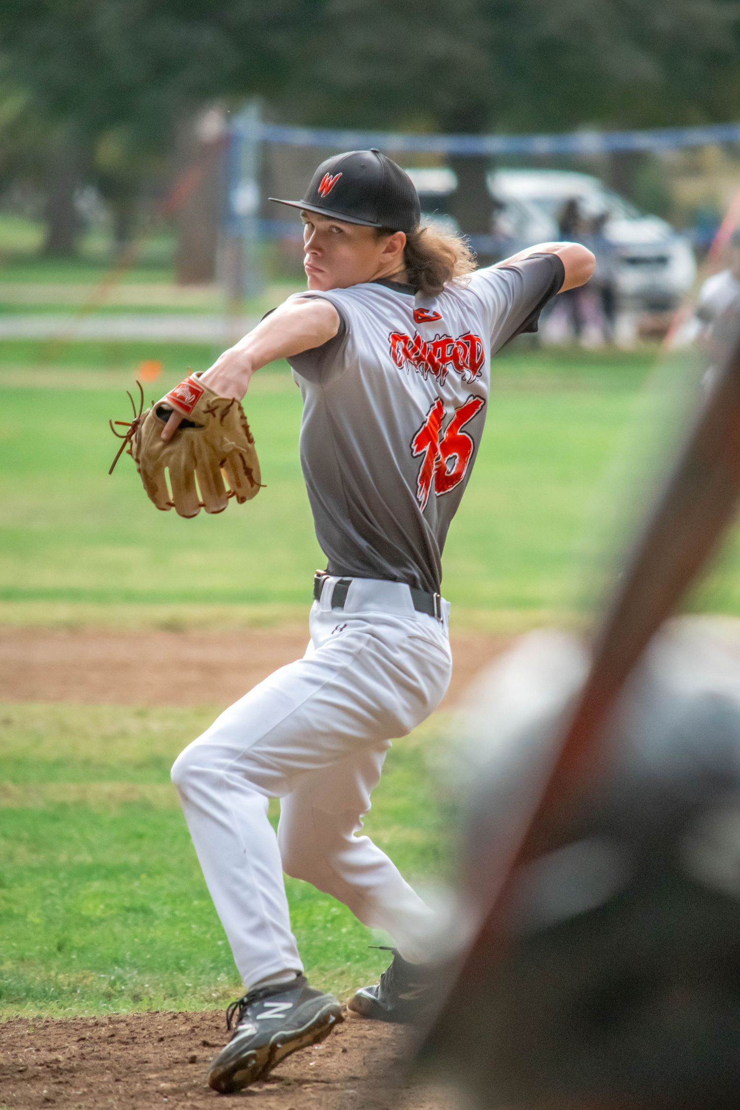 Baseball player in grey uniform winds up to pitch on grass field.