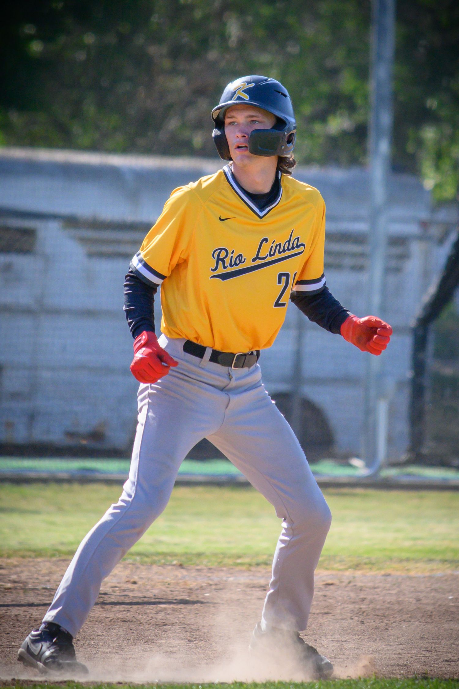 Baseball player in yellow jersey leads off base while preparing to steal during a game.