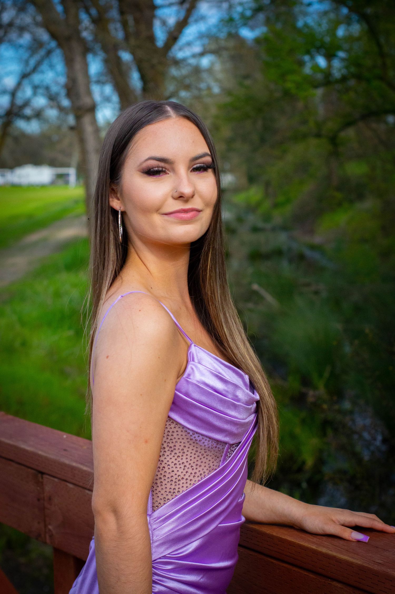 Woman in purple satin gown posing on wooden railing near water.