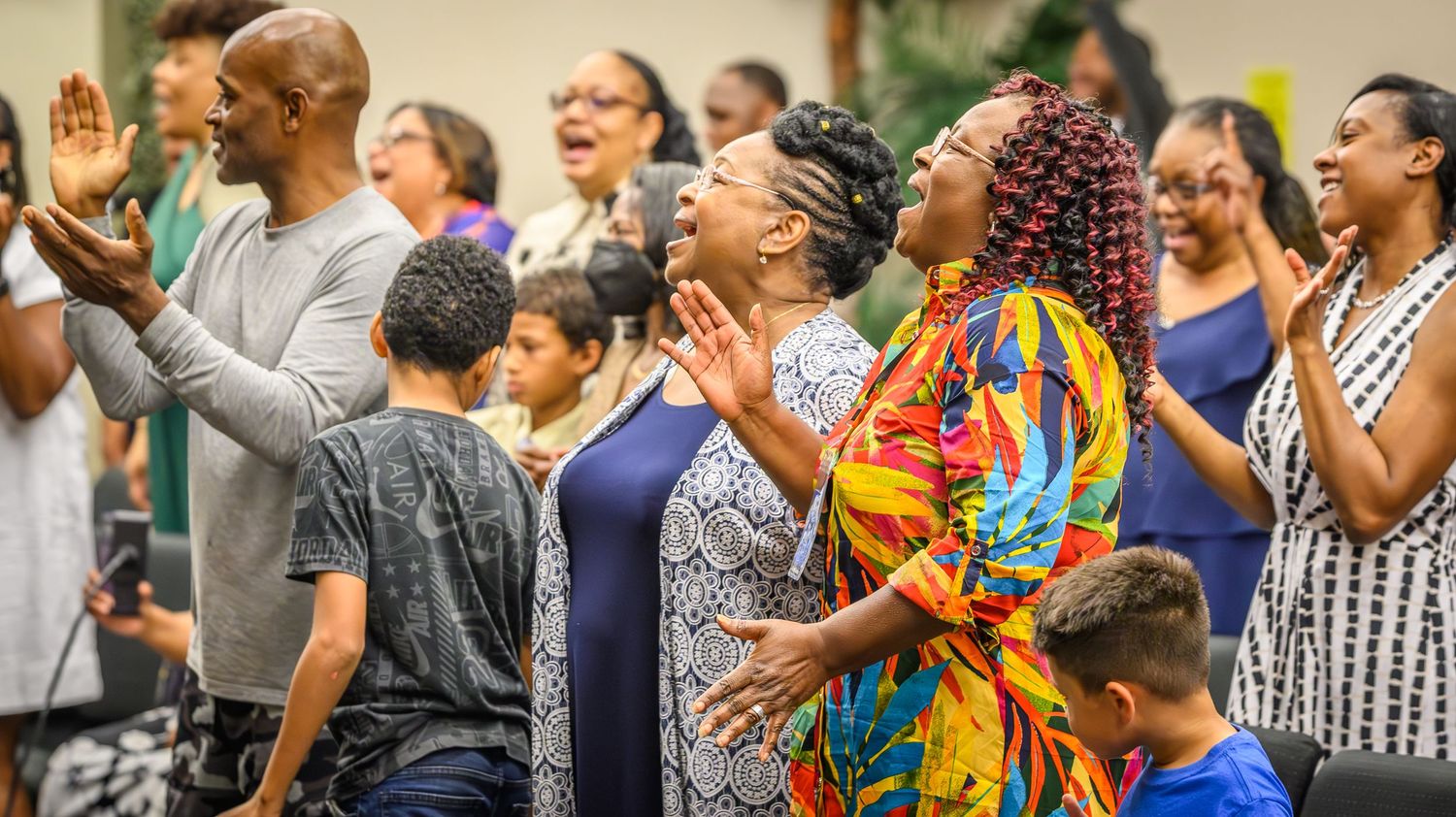 A crowd of people in colorful attire raise their hands in enthusiastic worship at a church service.
