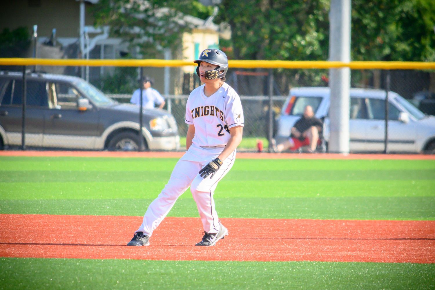 Baseball player in white uniform takes stance on red clay field during game.