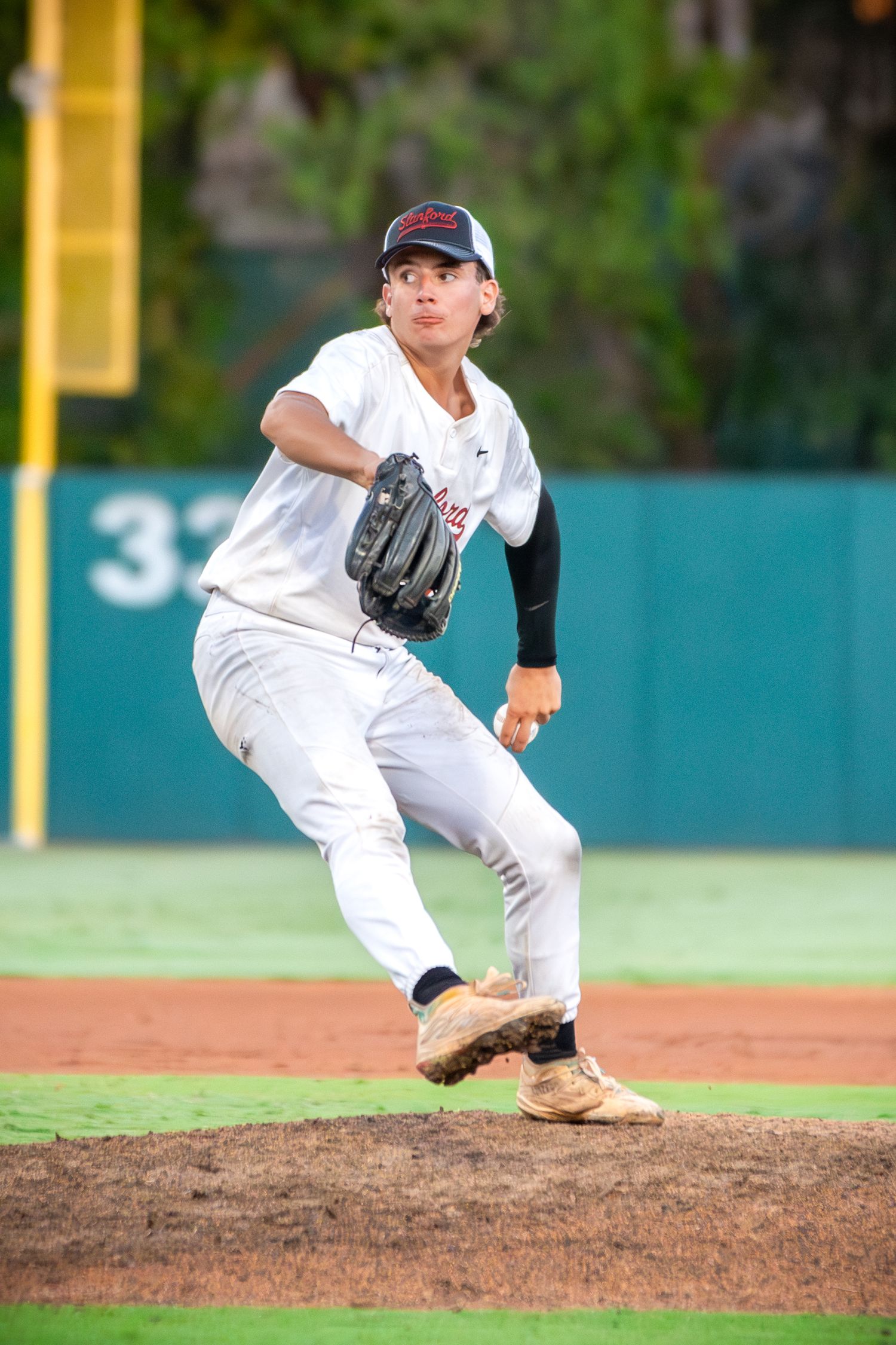Baseball pitcher on the mound follows through on delivery motion during game action on green field.