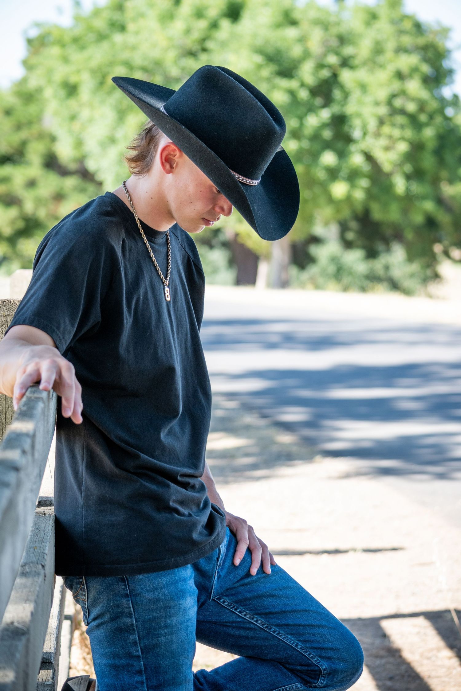 Country western themed photo shoot by wooden fence wearing black shirt and cowboy hat.