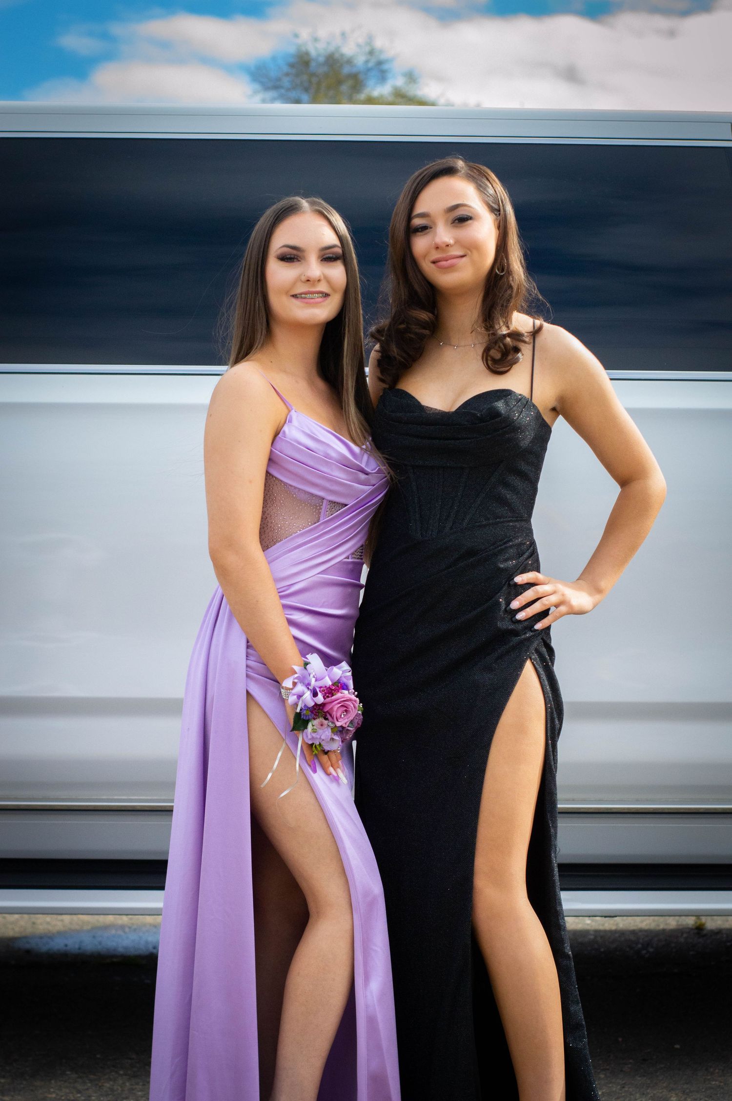 Two women in formal dresses posing together against a limousine.