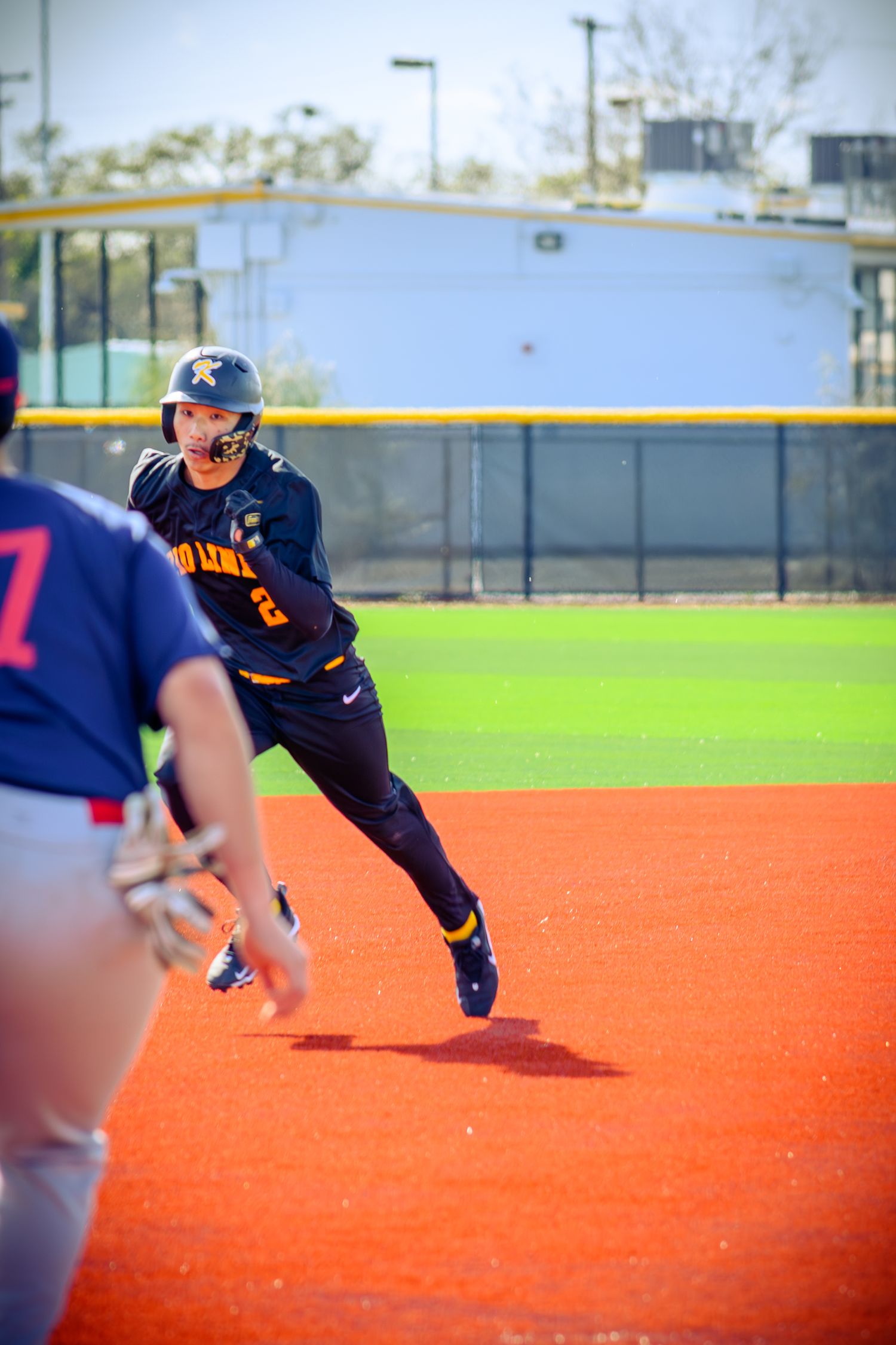 Baseball player slides across orange turf field in navy blue uniform during practice drill.