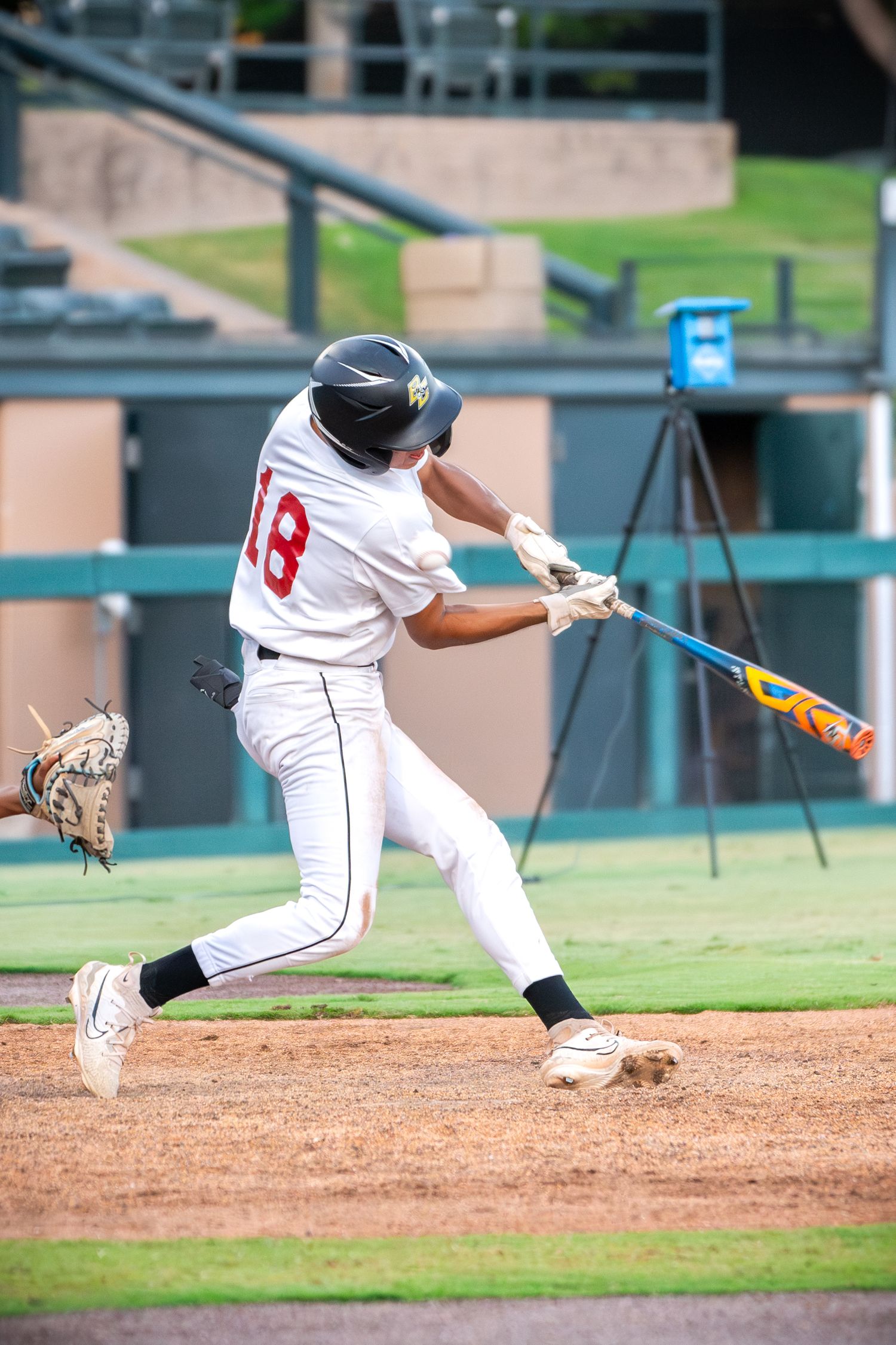 Baseball player in white uniform swings bat during game with focused batting stance at home plate.