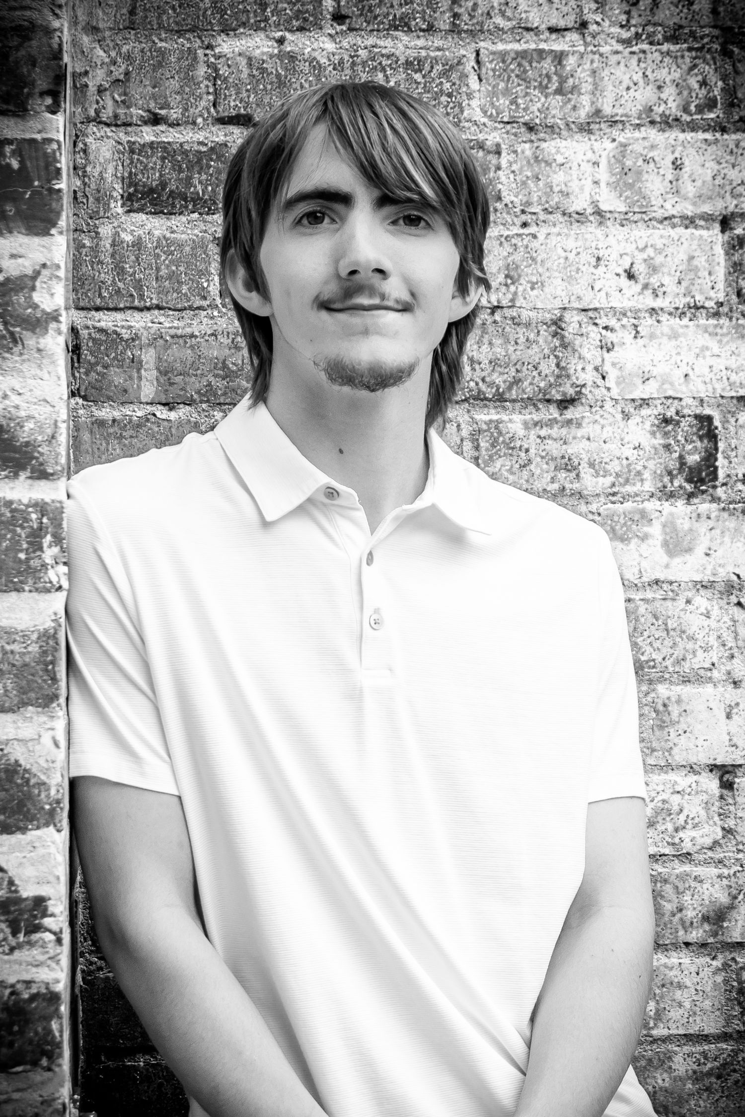 Black and white portrait against textured brick wall in white polo.