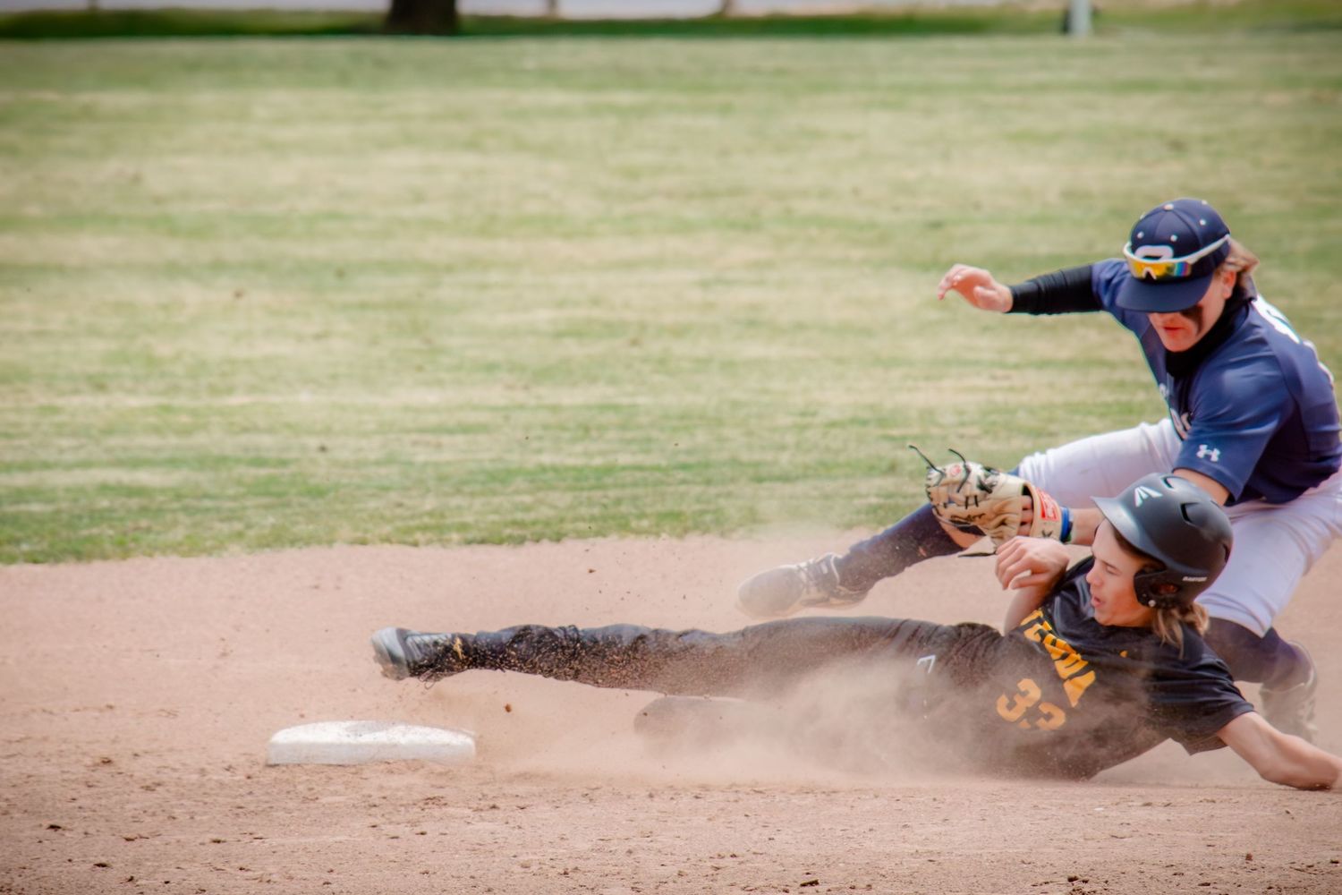 Action sequence of baseball players sliding and diving for base on dirt infield.