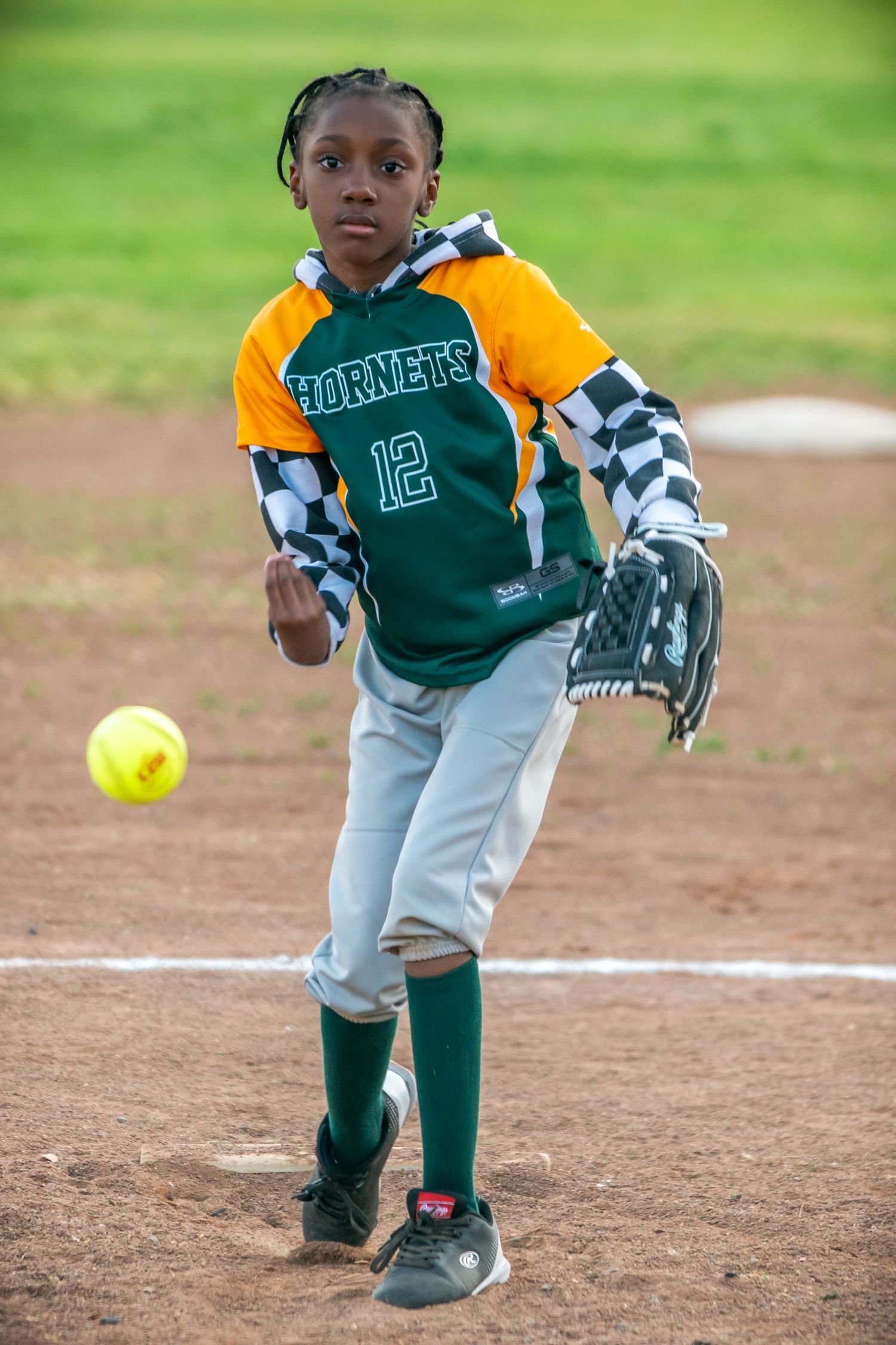 Little league player preparing to pitch softball on dirt mound during game.
