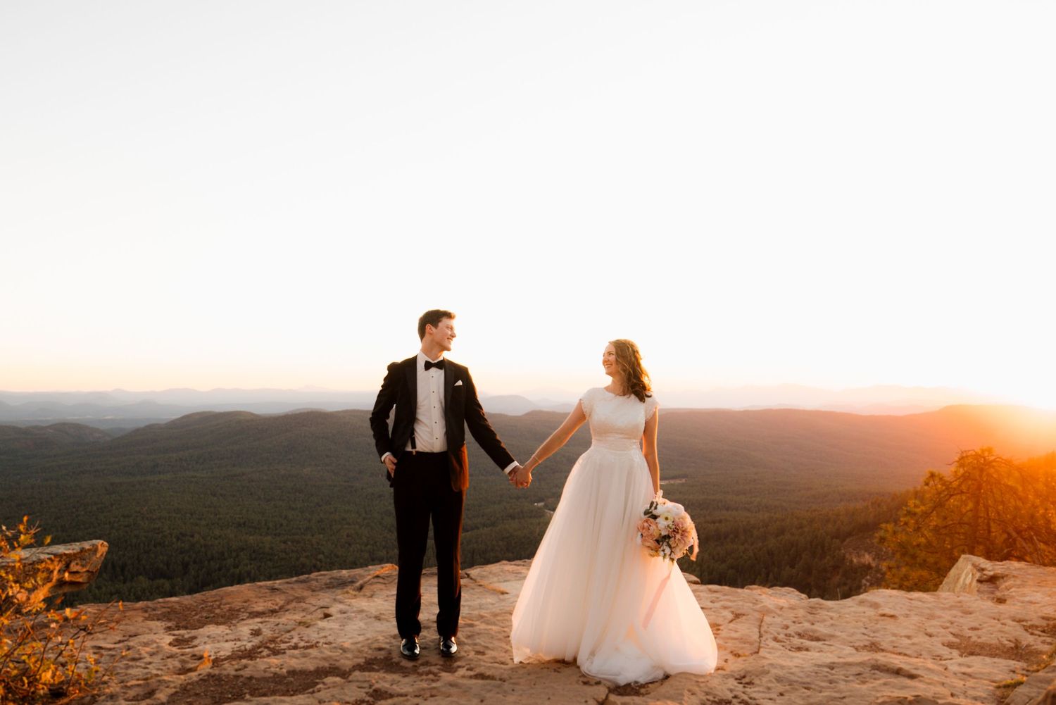 Couple shares intimate moments during golden hour wedding photography session on mountain summit at sunset.