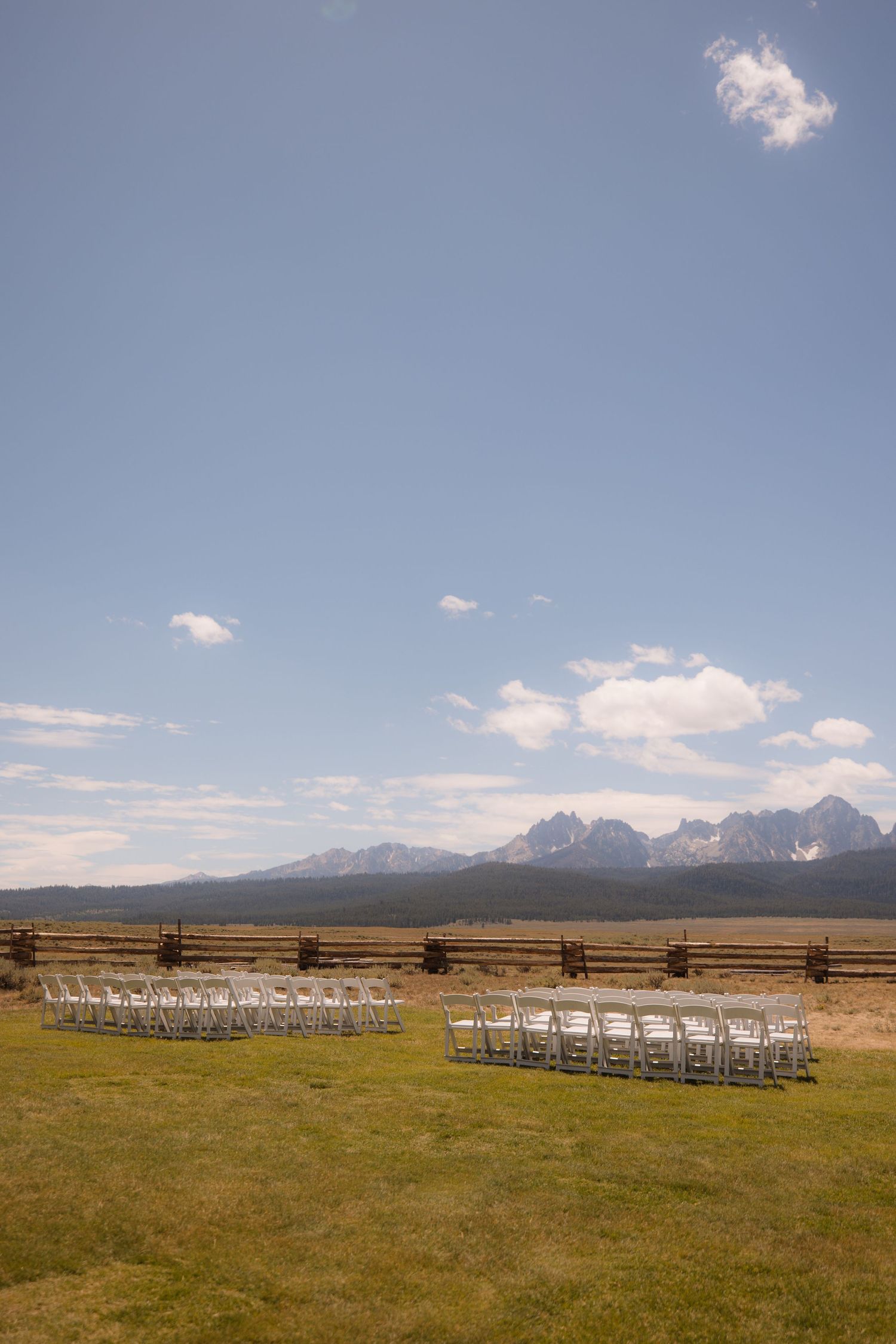 White chairs line a grassy meadow with majestic Grand Teton mountains rising in the background under a blue sky.