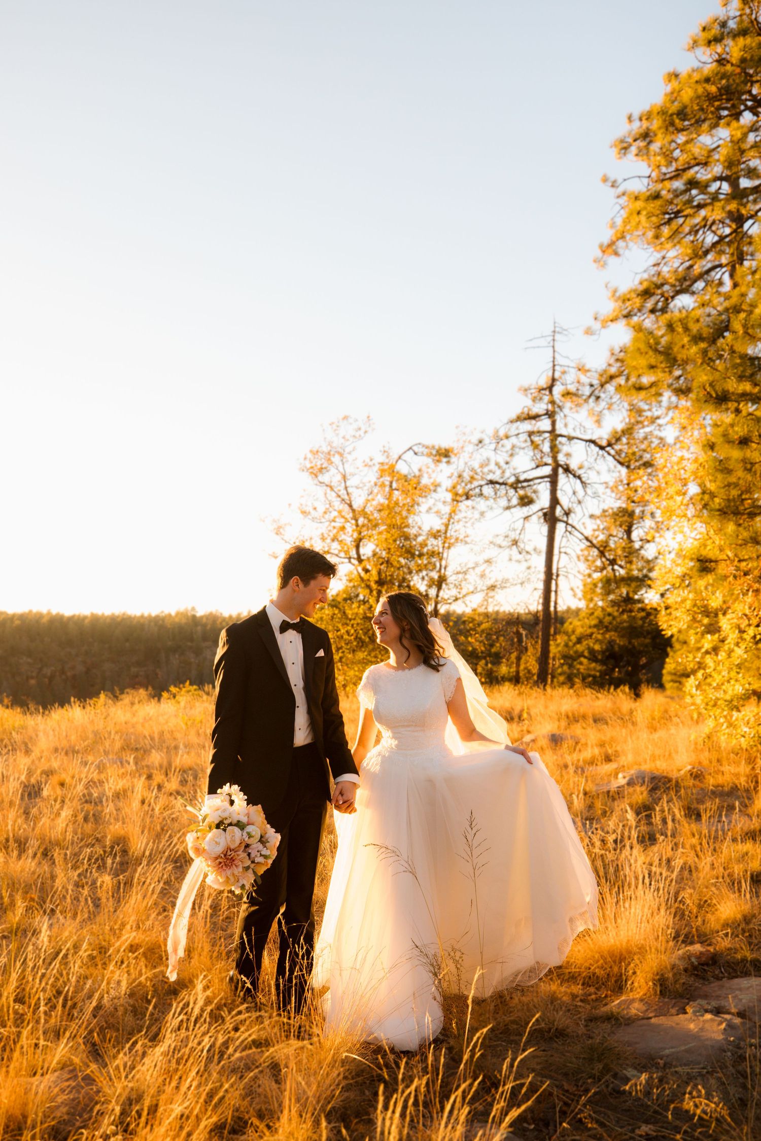 A couple walks through golden autumn field at sunset creating romantic silhouettes against warm light.