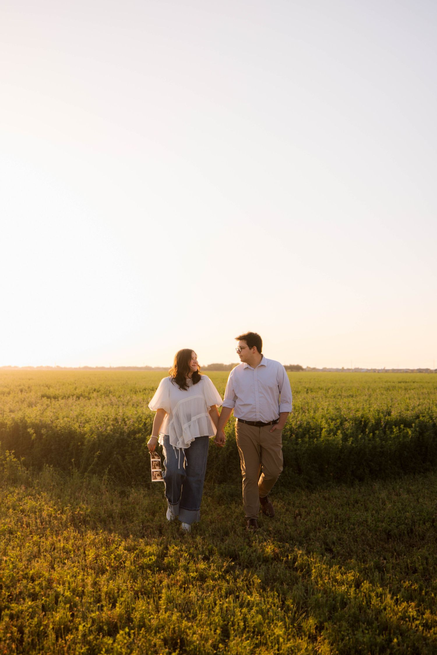 A couple walking hand in hand through a field of yellow wildflowers during golden hour.