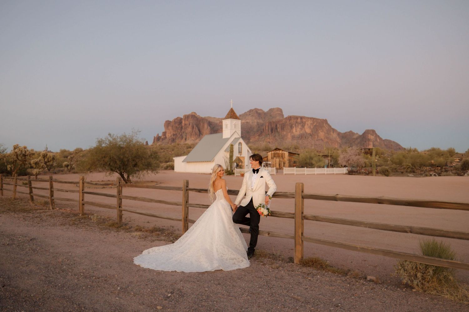 A romantic couple walks along a wooden fence at sunset in front of the desert mountains of Arizona.