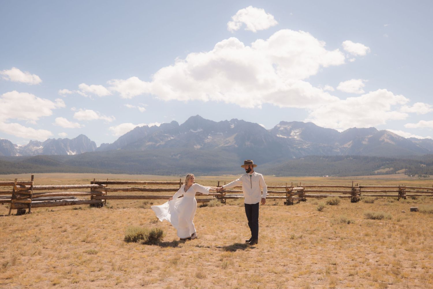 A panoramic view of mountains and rural ranch land with wooden fences stretching across the golden prairie landscape.