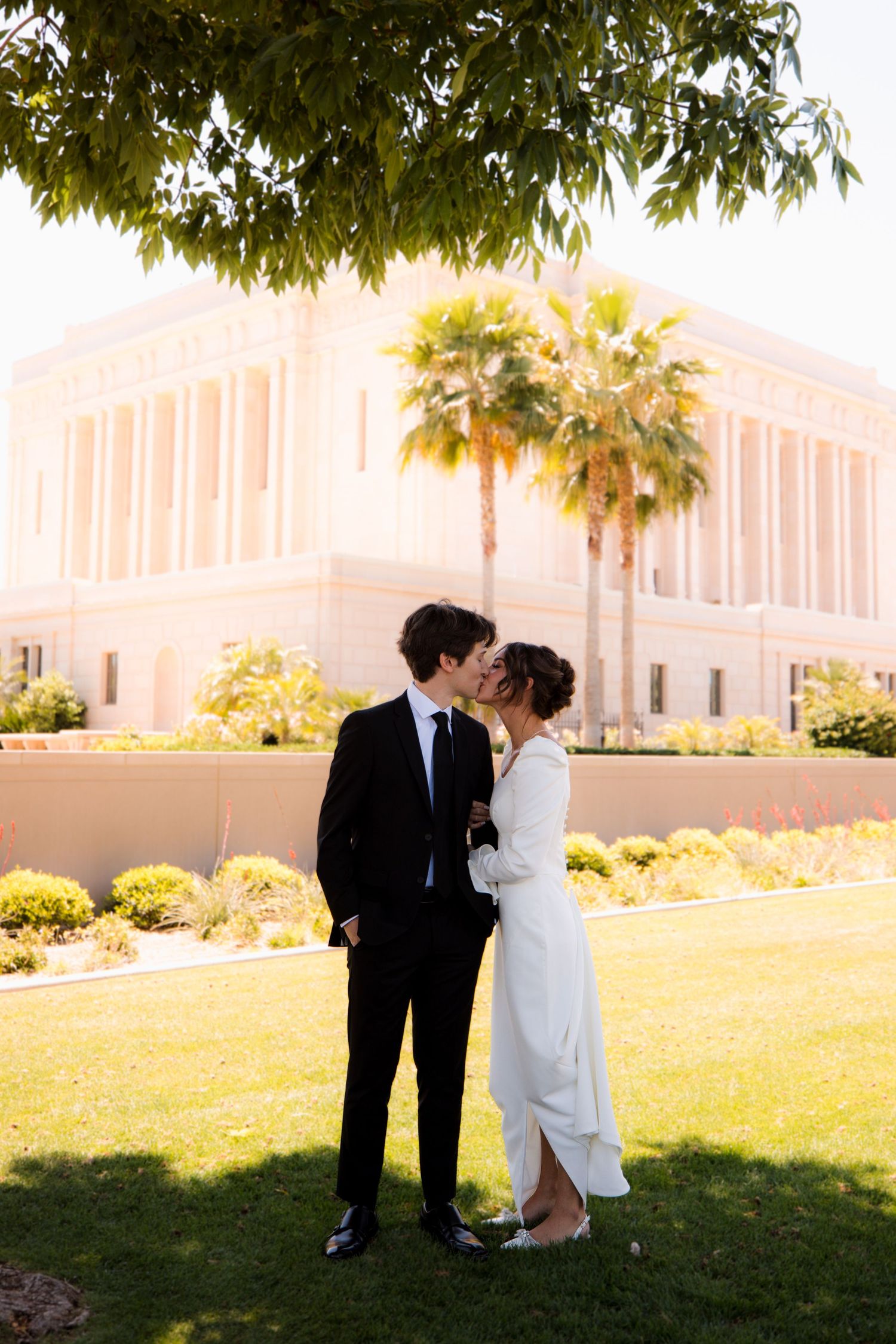 Wedding couple embraces in silhouette against a temple building backdrop on a sunny afternoon.