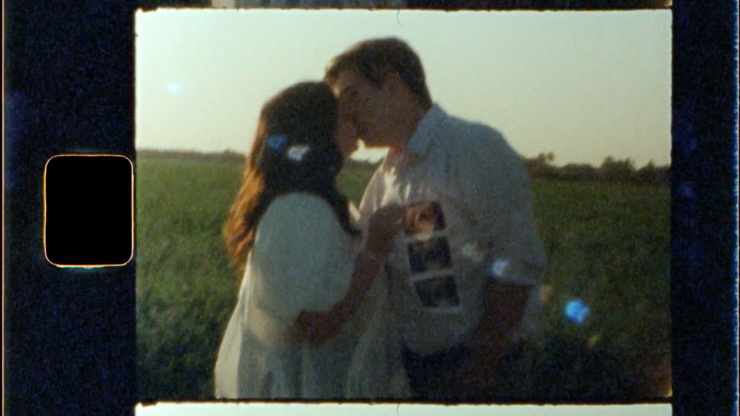 Two people share a tender moment at sunset in a golden field with mountains visible in the background.