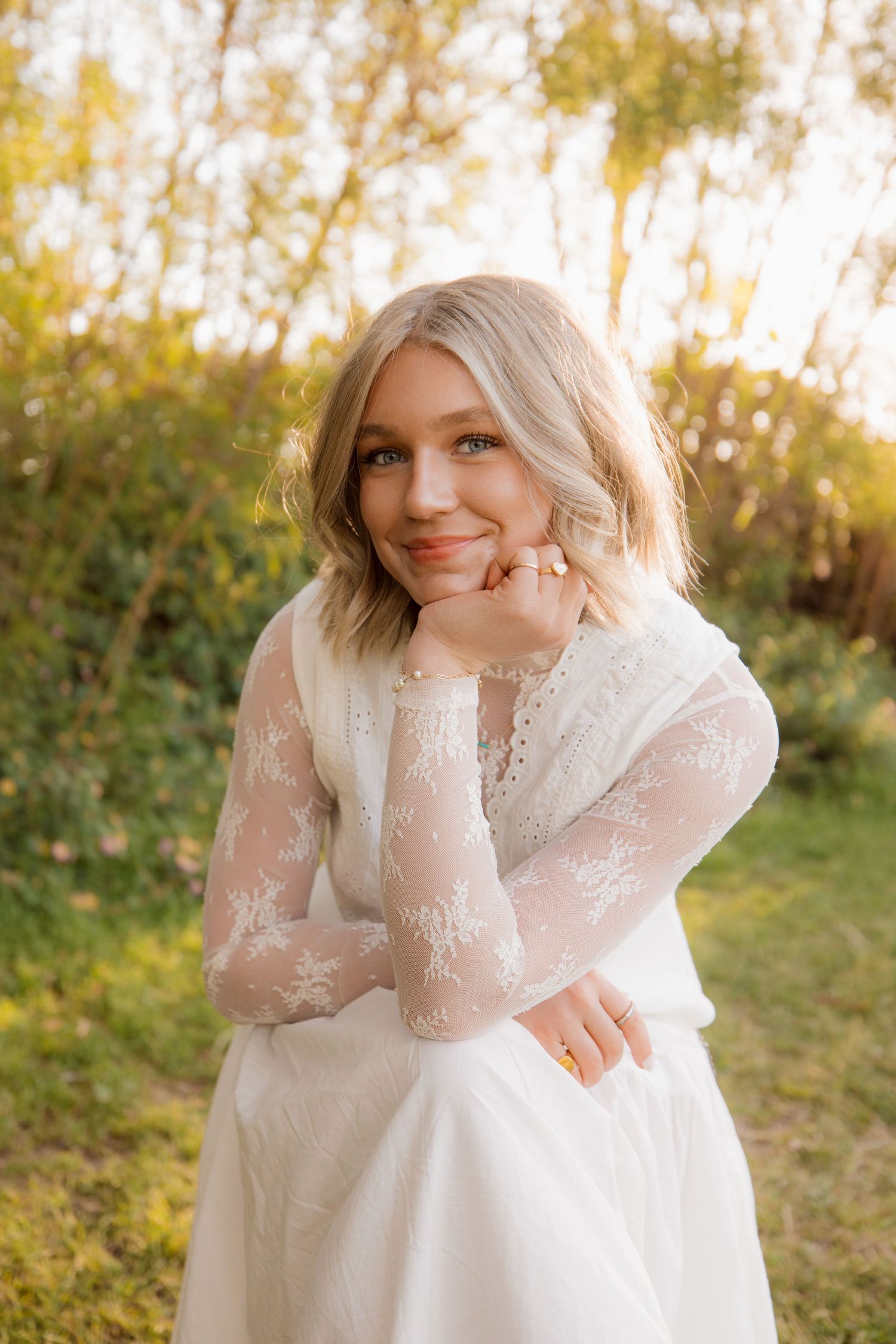Person in white lace dress sits in golden sunlight during outdoor autumn photoshoot.