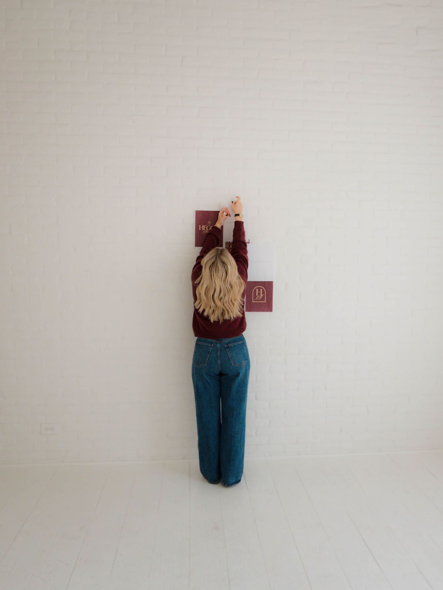 A sequence of minimalist photos showing a person in teal pants against a white wall viewed from progressively farther distances.