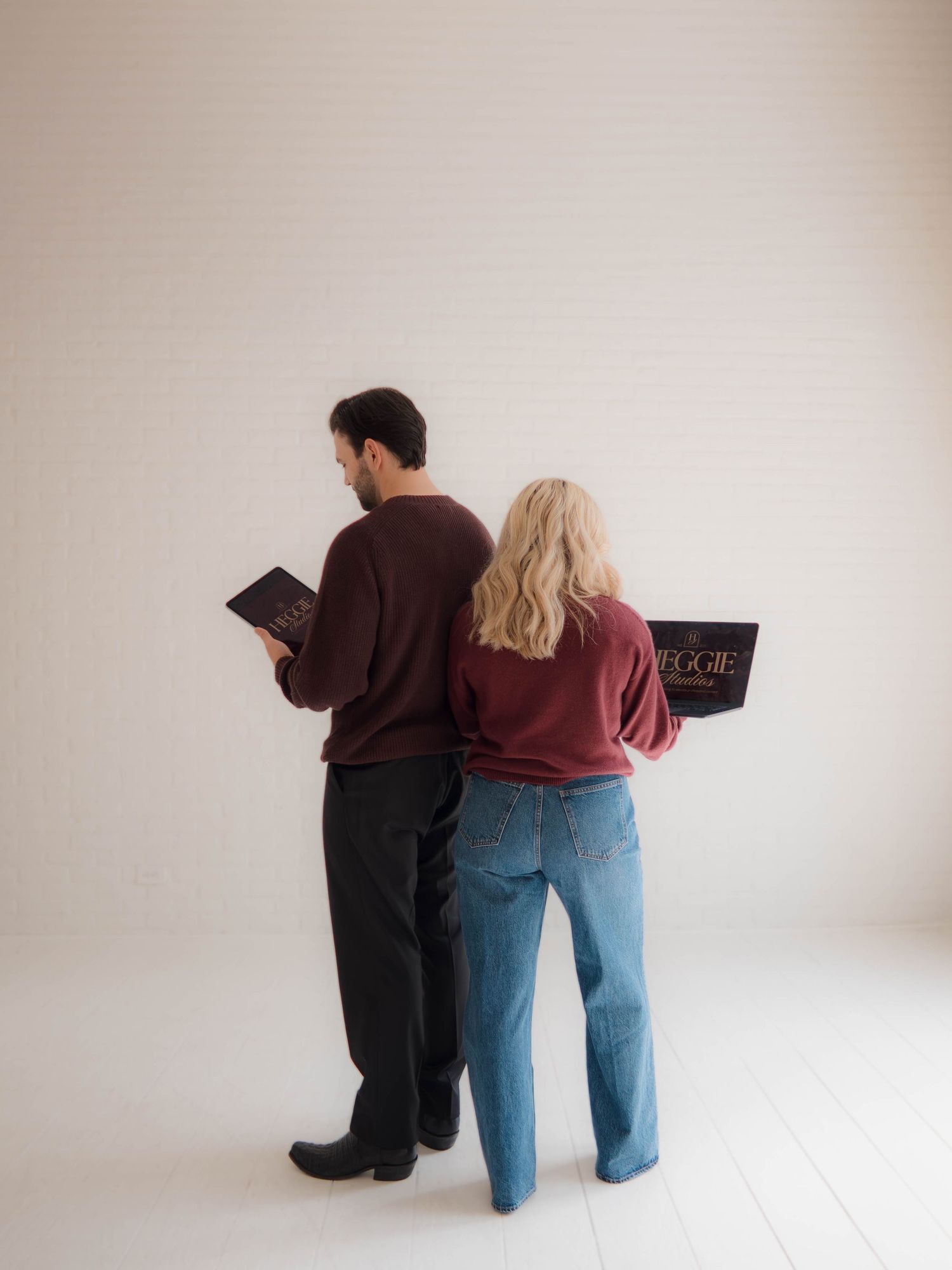 Two people in casual attire read books while sitting together against a light-colored wall.