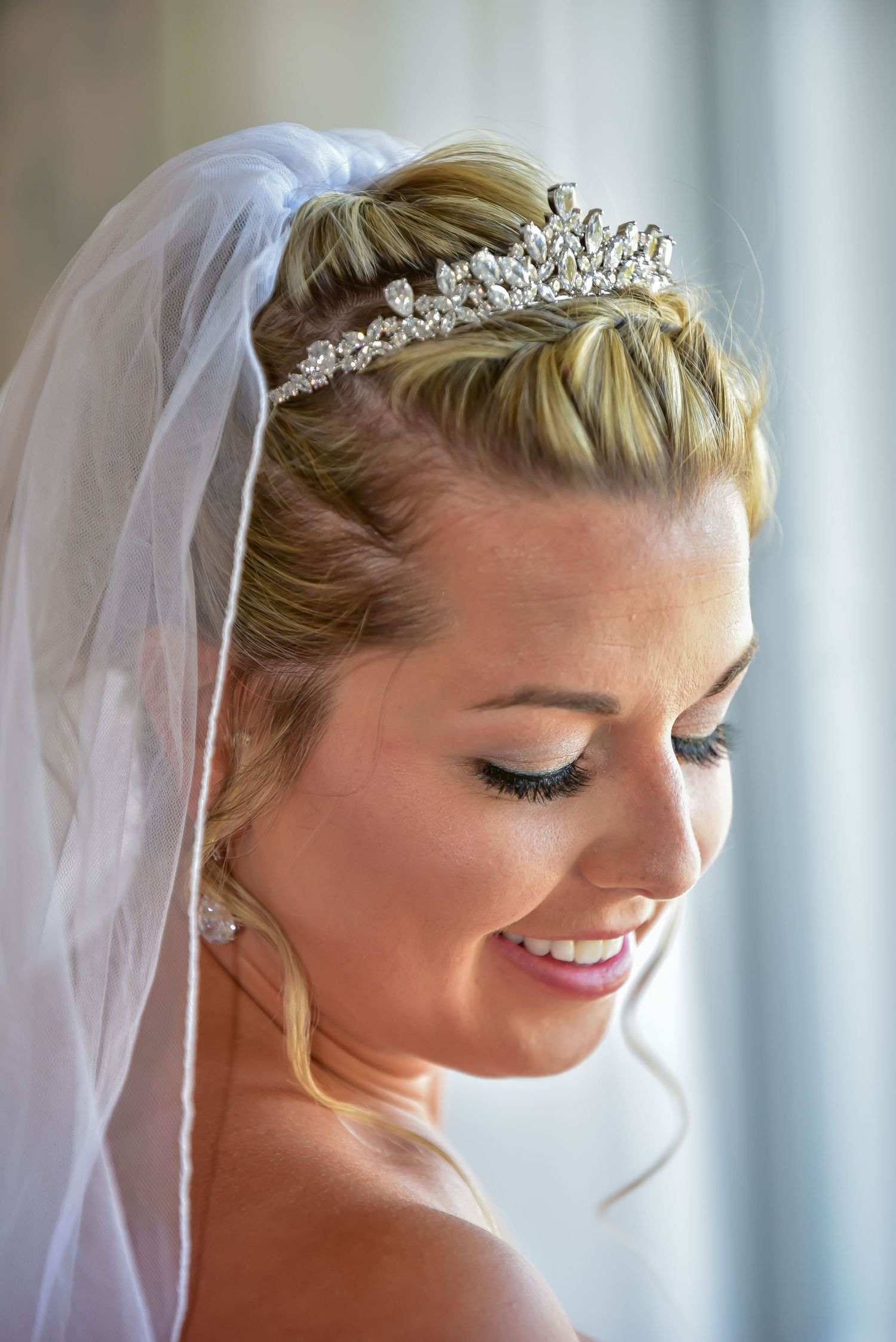 A blonde bride wearing a veil, looking down toward her shoulder with a smile. Taken by Vazul Studios.