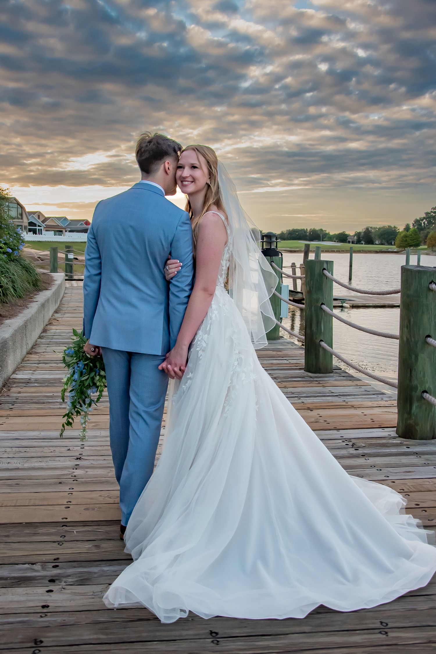 Wedding couple on wooden dock at sunset with dramatic cloudy sky.