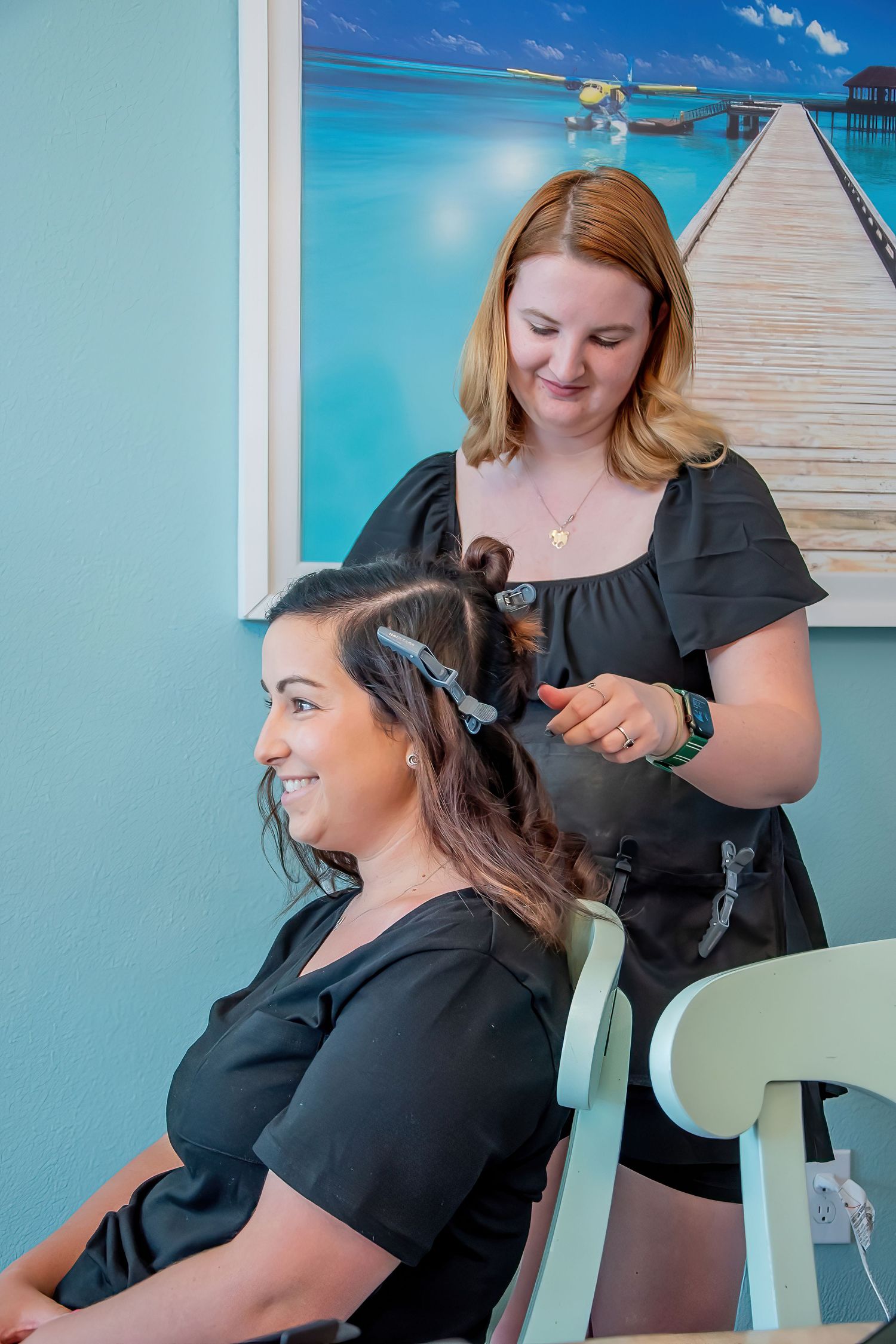 Hair styling session with stylist working on client's hair against blue wall background.