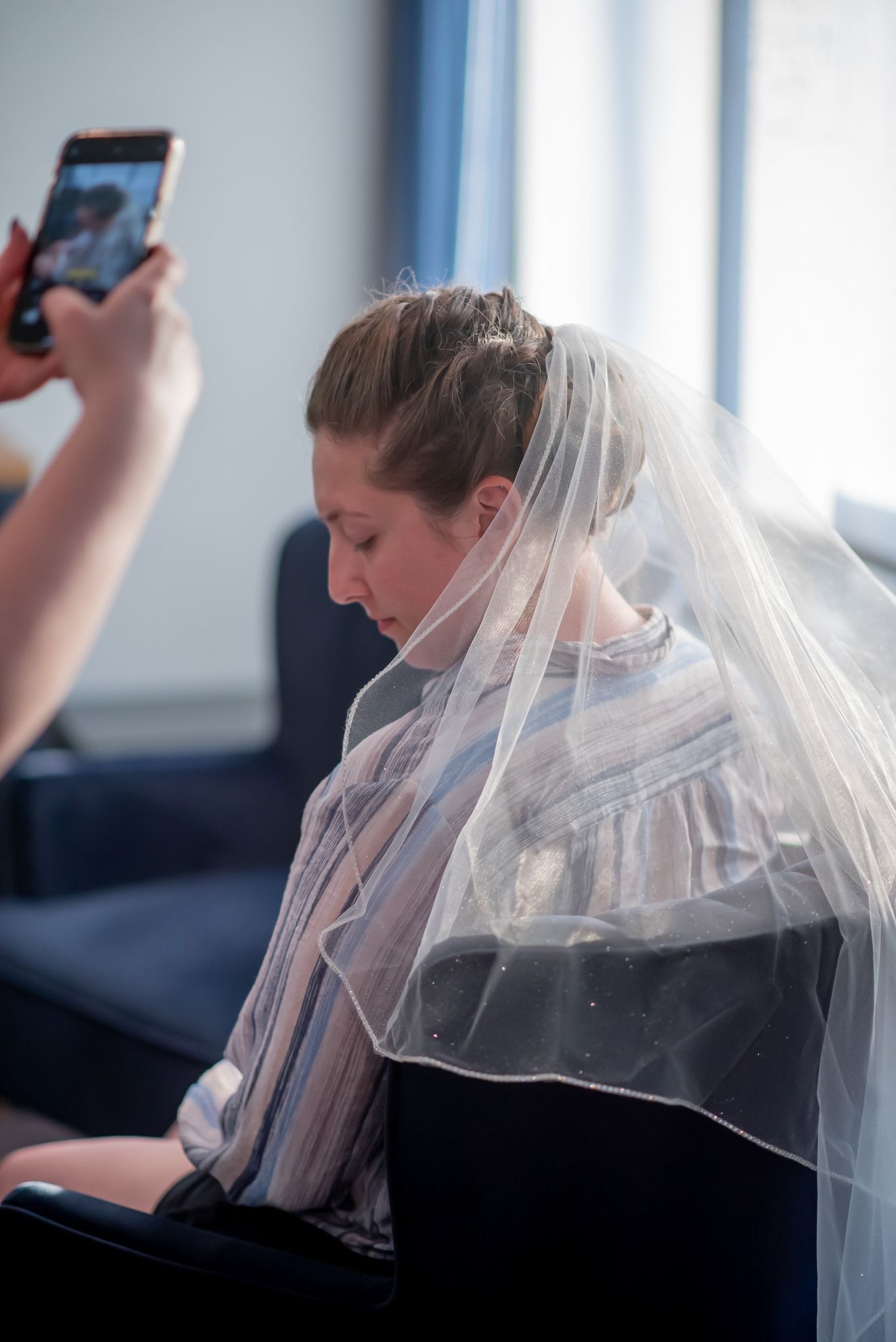 Photo in an Ocala, FL salon of a stylist taking a photo with her phone of a bride with her hair done, wearing a veil.