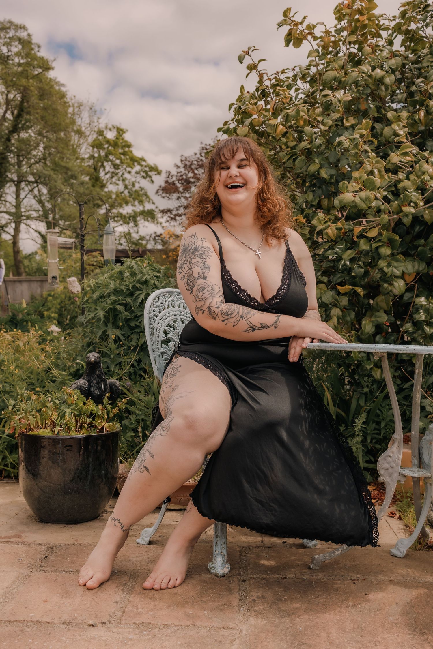 Laughing Tattooed, plus size woman posing with a Japanese fan amongst some flowers, outdoors confidence boosting boudoir photography Suffolk