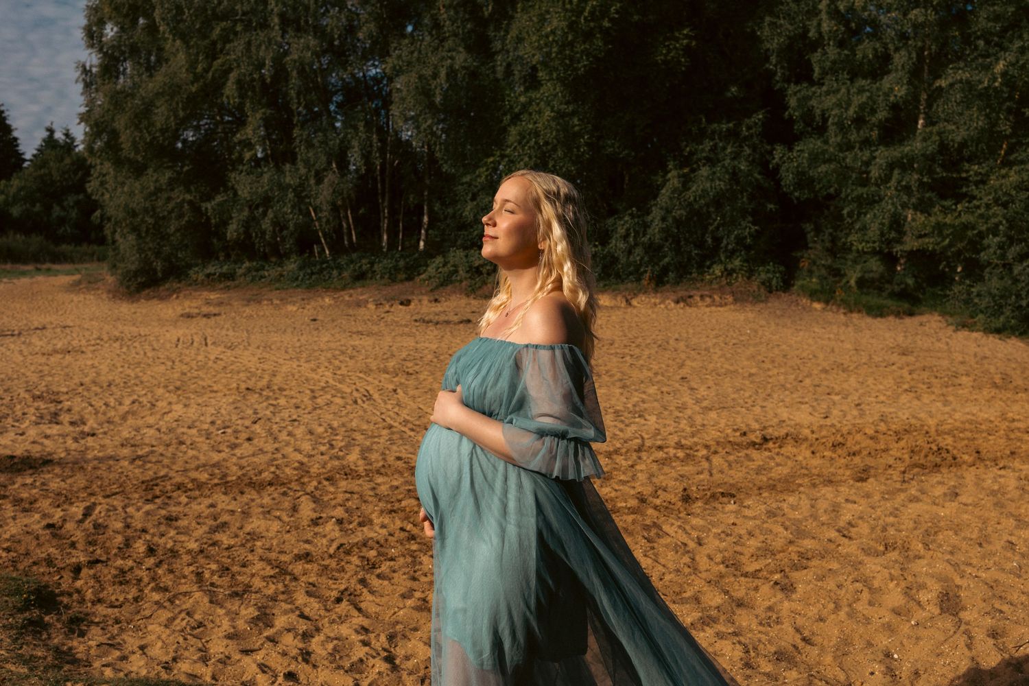 Outdoor maternity portrait of woman in blue dress walking in he sand, sun kissing her face , beautiful