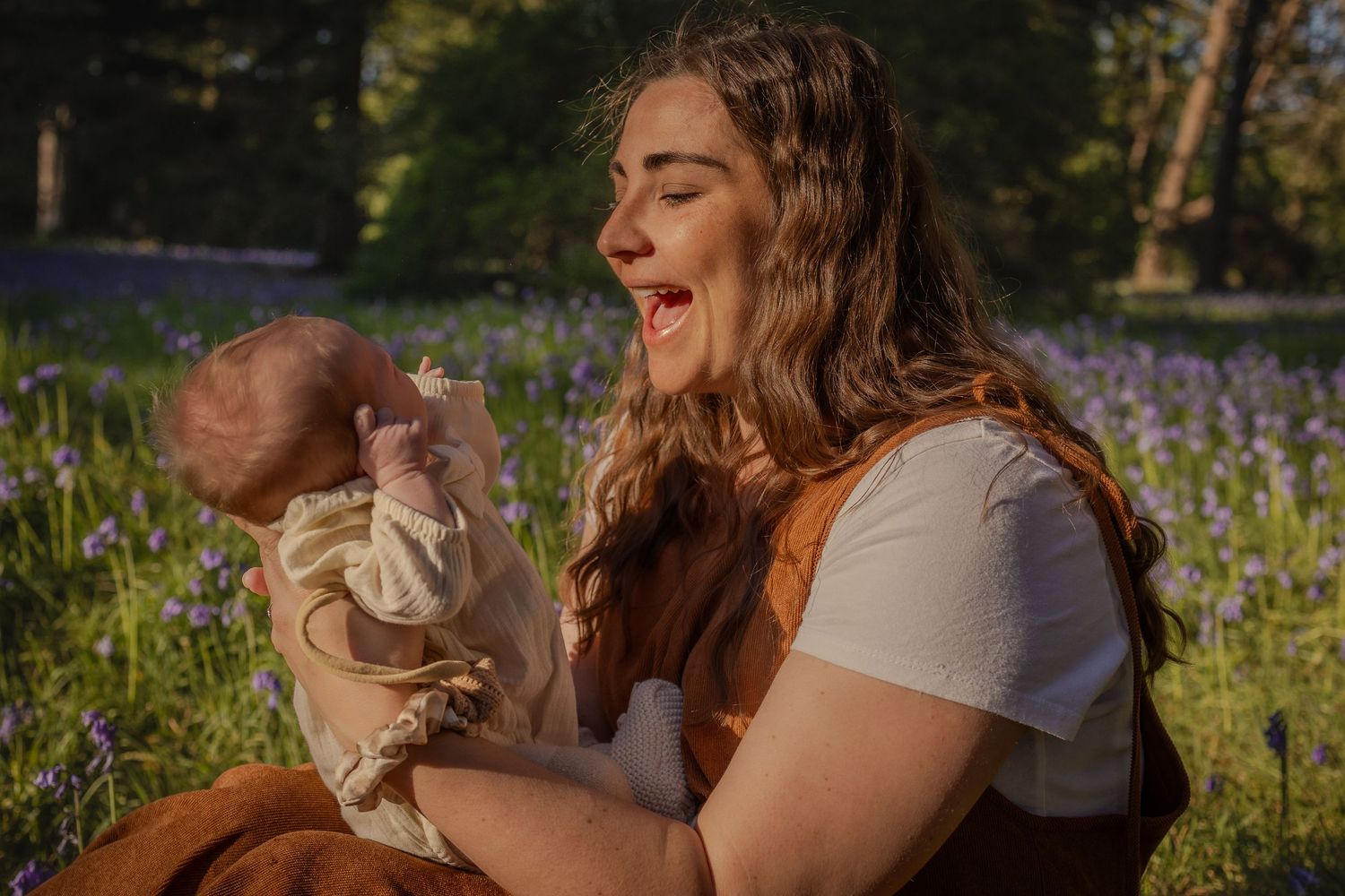 Portrait of moment of connection between mother and newborn in a bluebells field at sunset in Norfolk by Untamed Muses