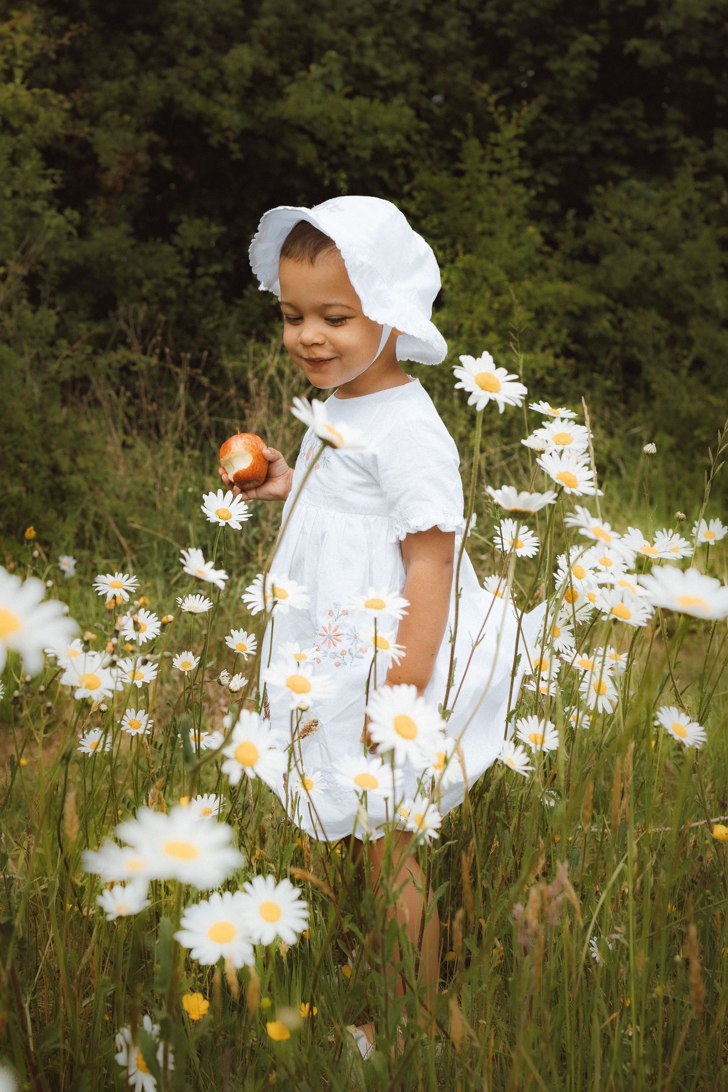 Portrait of toddler eating an apple in a field of daisies in Norfolk by Untamed Muses