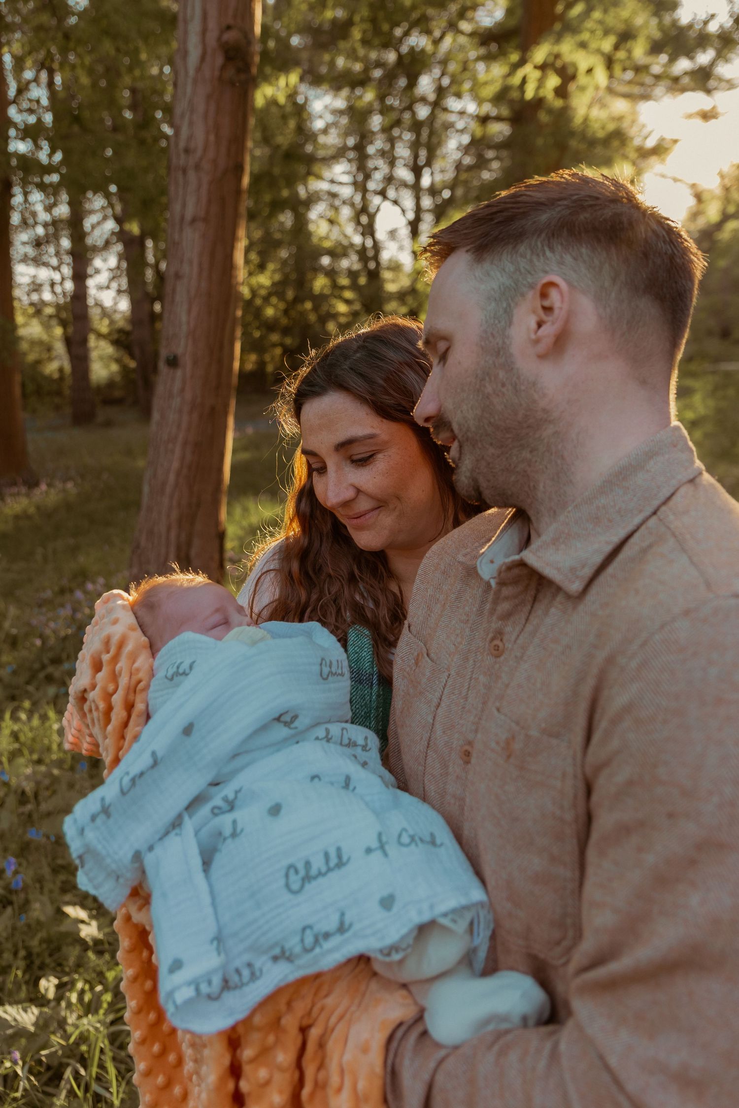 Evening, spring outdoors natural newborn photoshoot, portrait of parents holding newborn daughter gapingly lovingly upon her