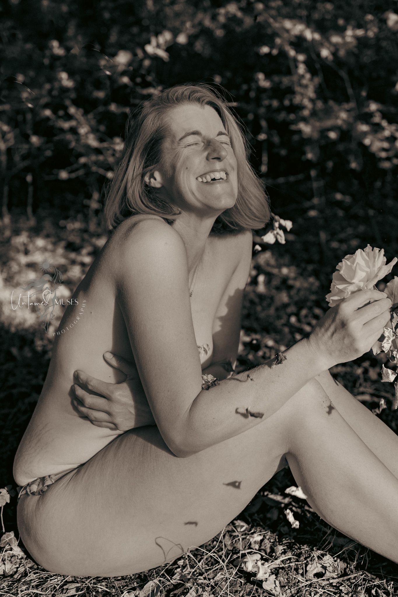 Monochrome portrait of mature lady during a boudoir session in nature, laughing, at one with her surroundings. Body confidence boudoir