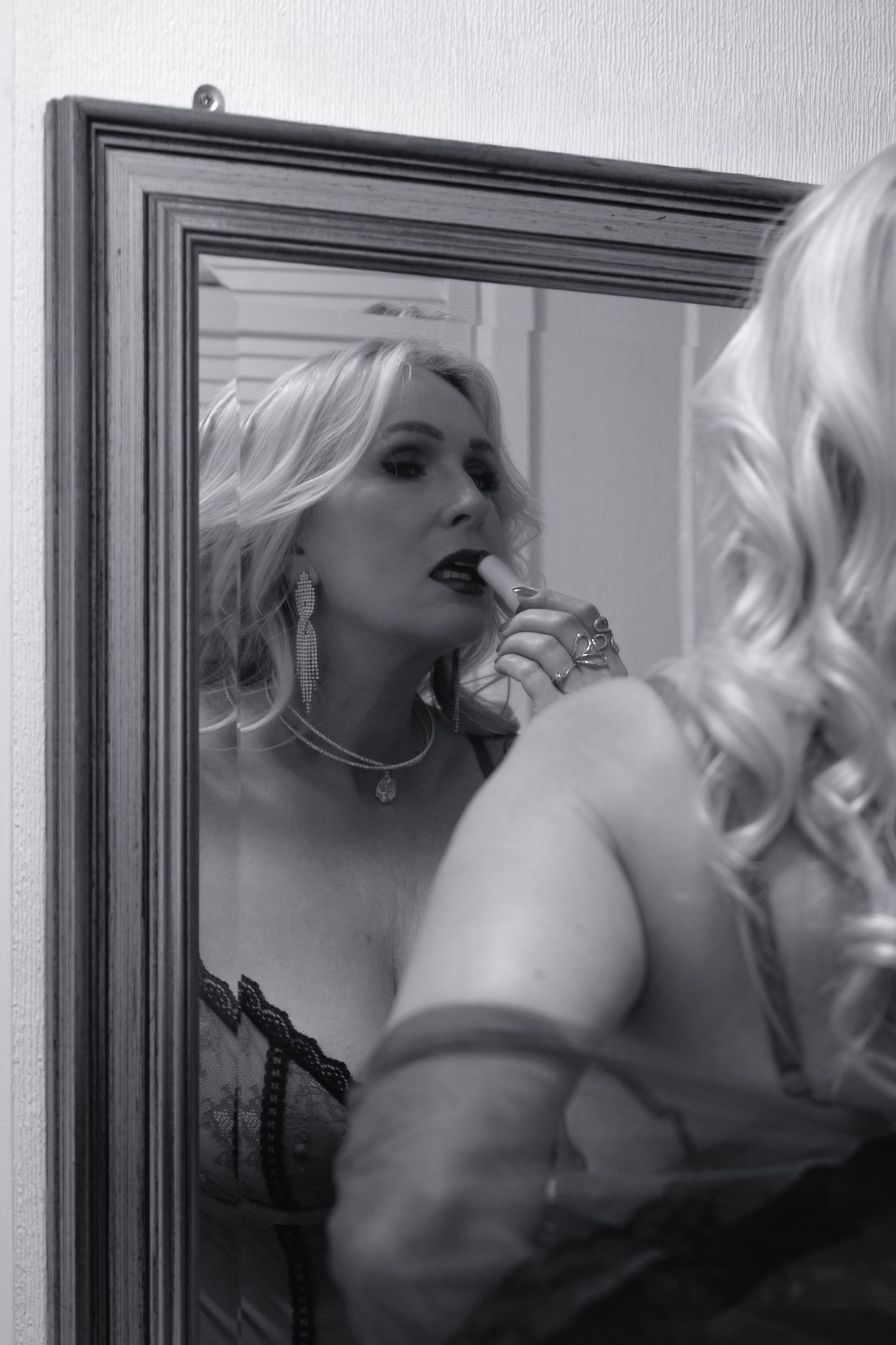 Monochrome portrait of mature beautiful woman putting lipstick on in front of a mirror during a boudoir confidence building photoshoot