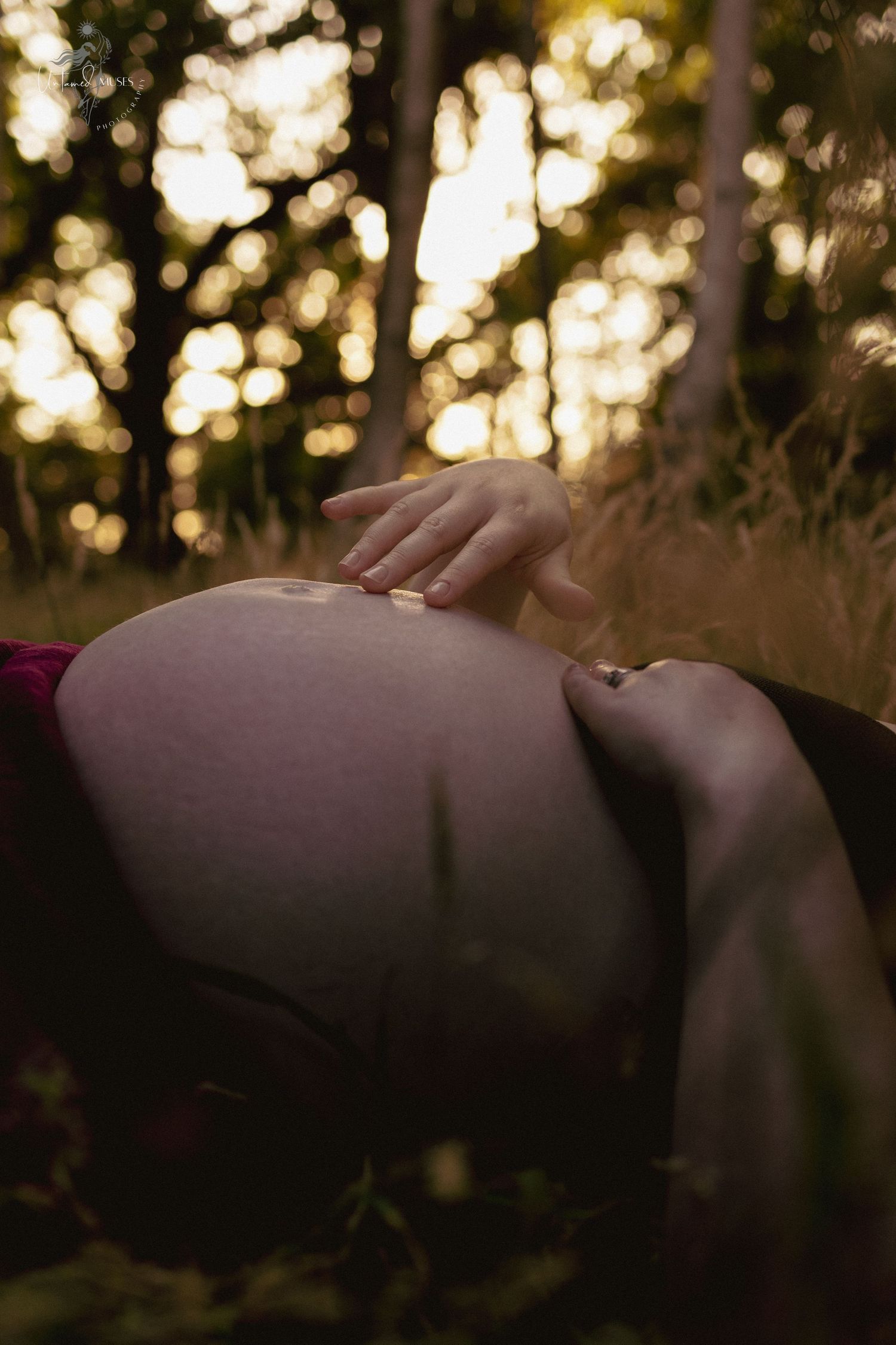 close up portrait detail of pregnant belly, and mum running her fingers through the skin, low sunlight, in the woods, Norfolk