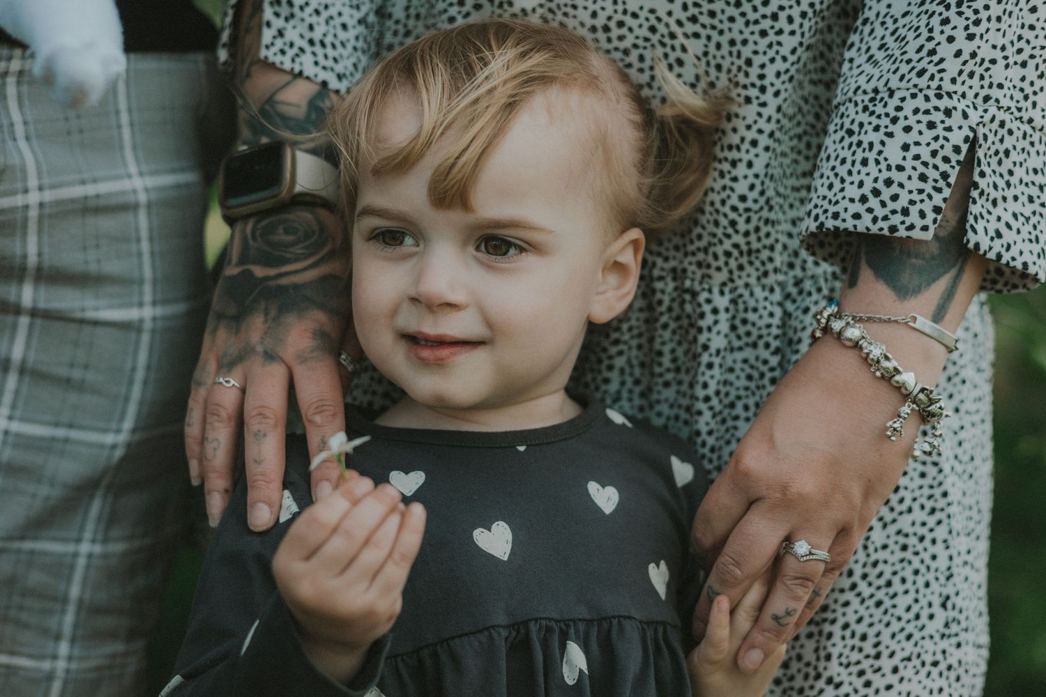 Close up of a family portrait, featuring tattooed hands of parents and child holding flower looking into distance, Suffolk, Untamed Muses
