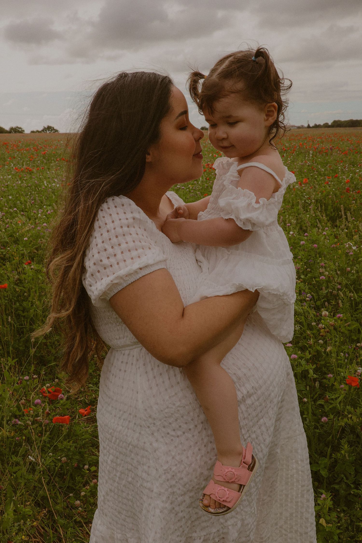 Maternity photography outdoors in a poppy field, featuring a mother and her toddler daughter and bump sharing a sweet connection moment